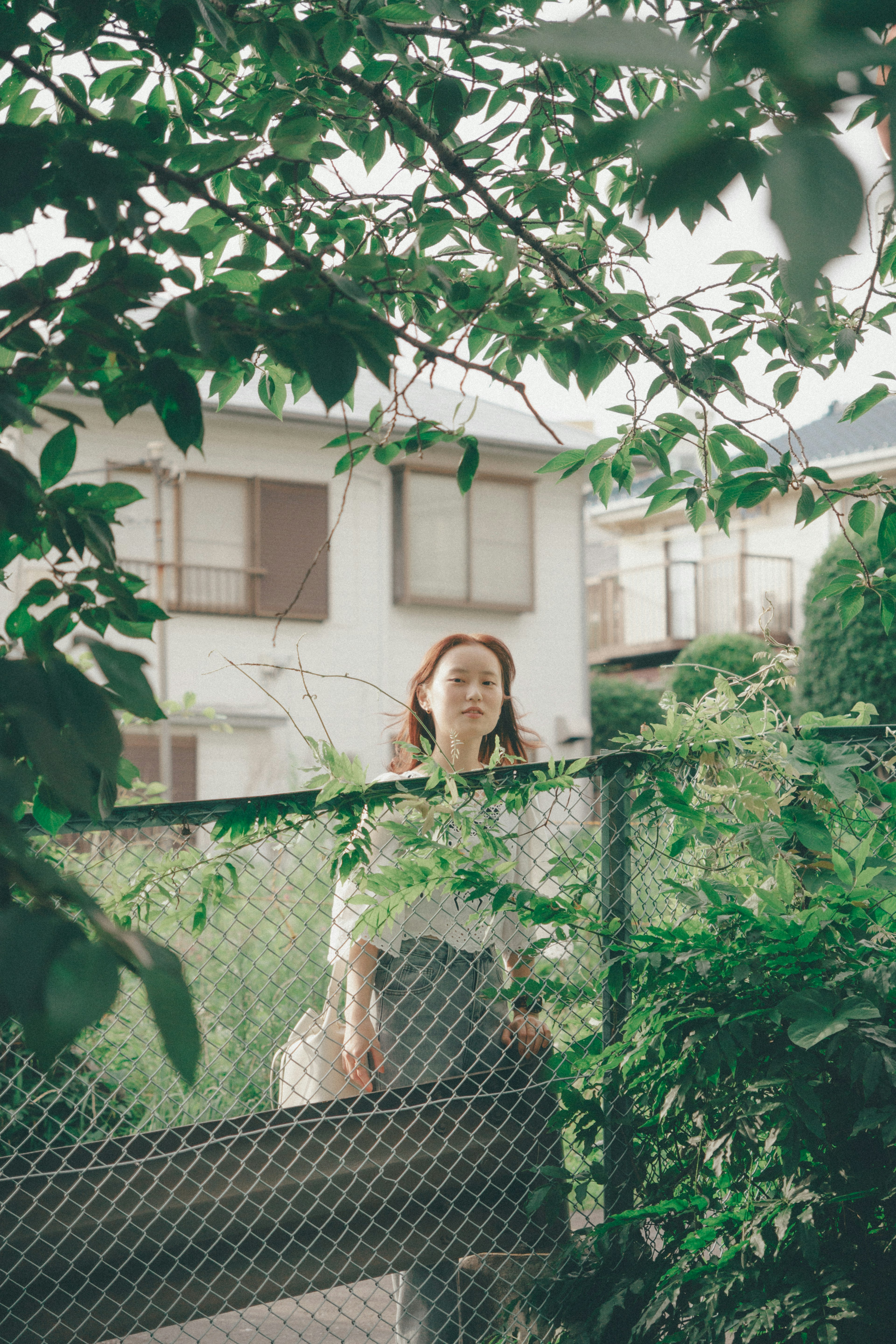 A woman standing in front of a fence surrounded by green leaves