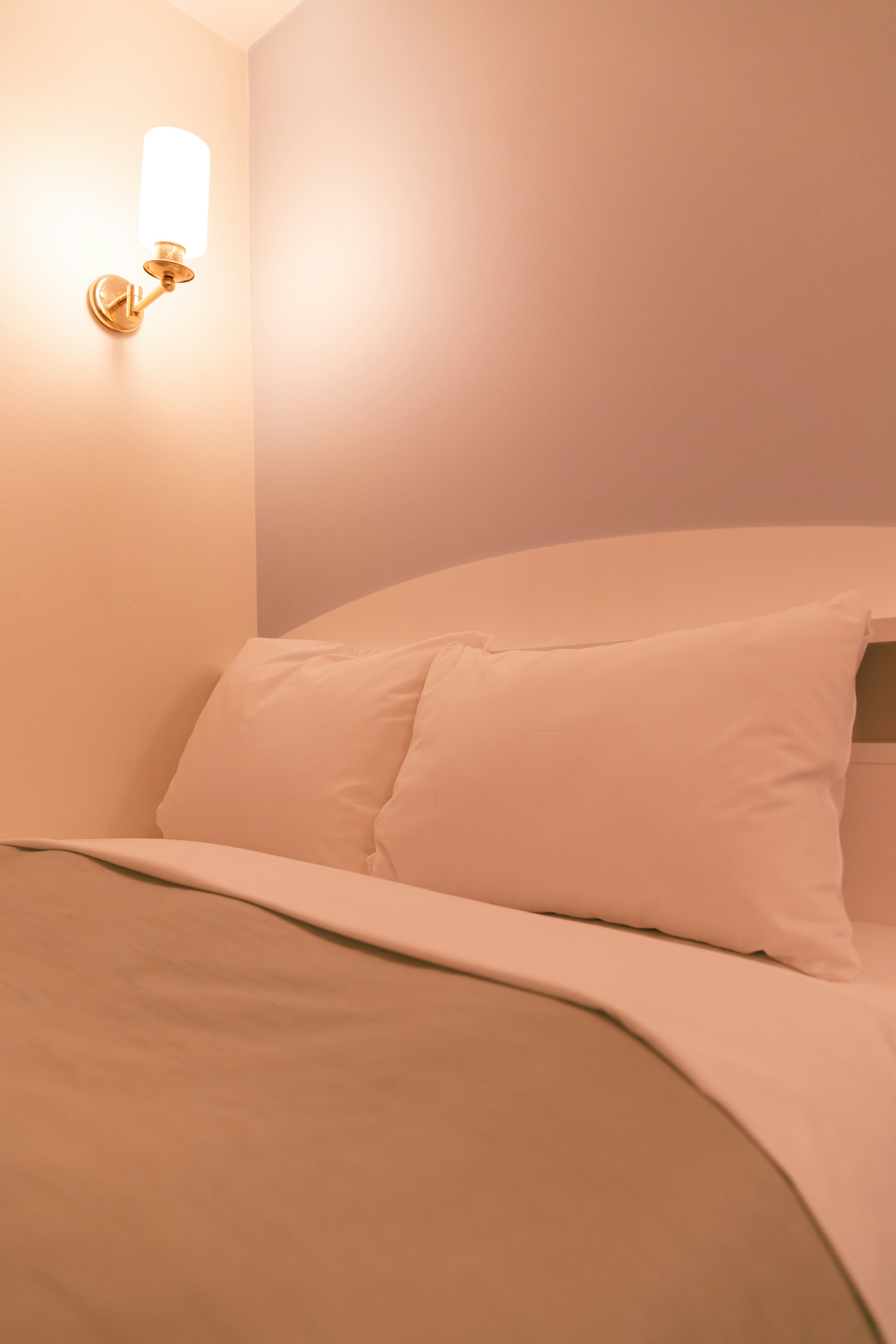 A cozy bedroom corner featuring a bed with soft pillows and a stylish wall lamp