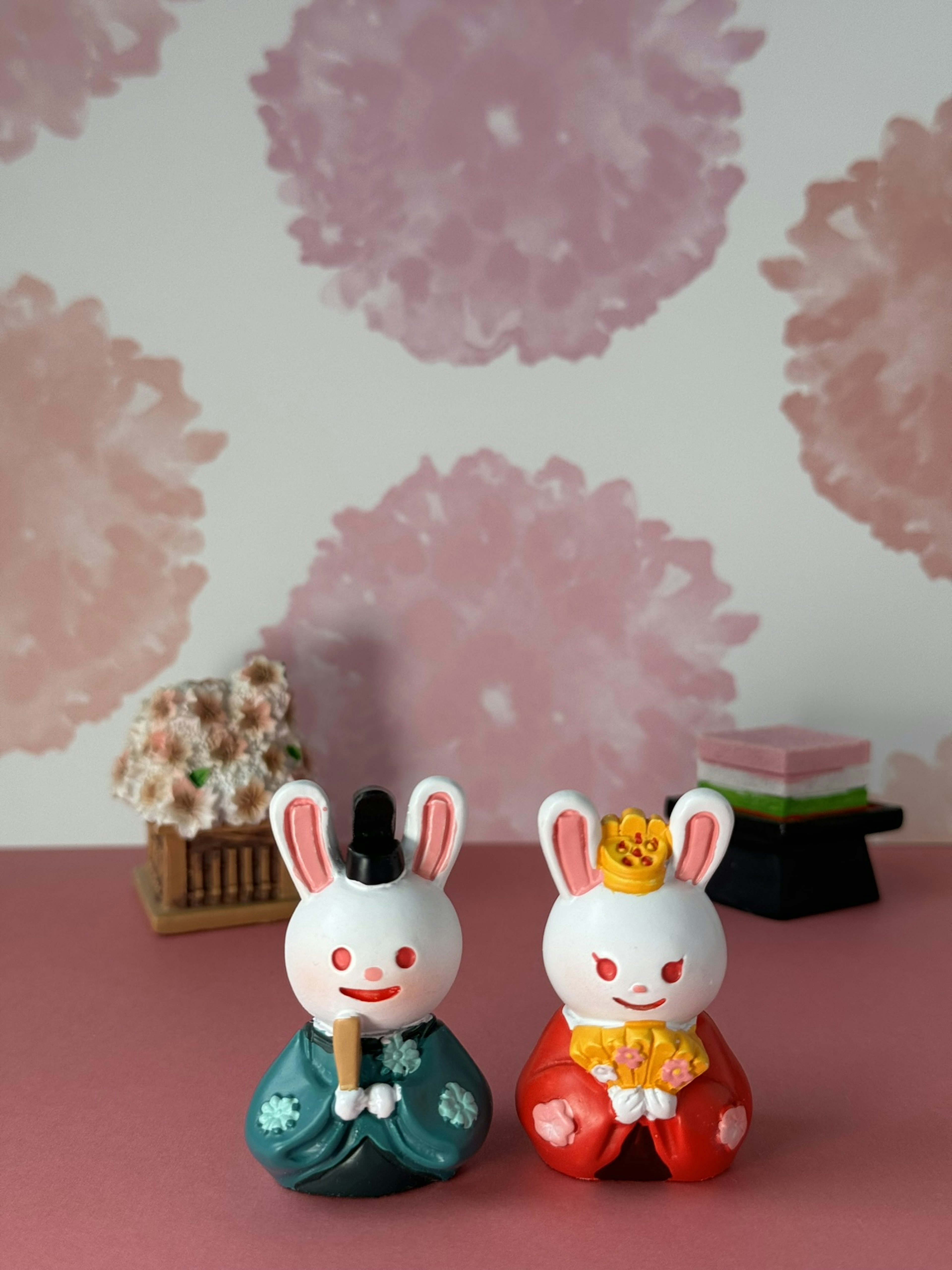 Two decorative rabbits in traditional clothing against a soft pink watercolor background