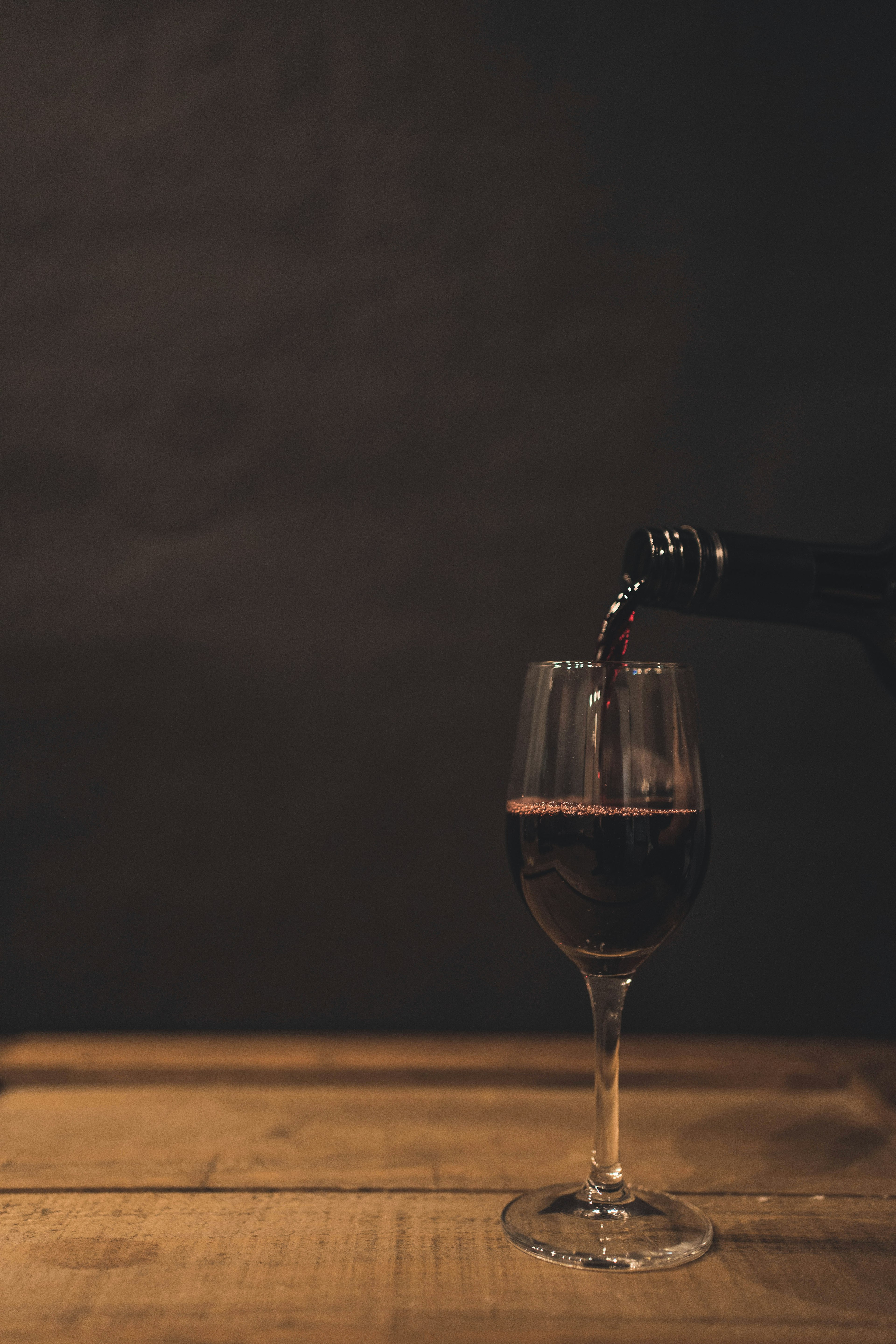 Una escena de vino tinto vertido en una copa con un fondo oscuro y la copa sobre una mesa de madera