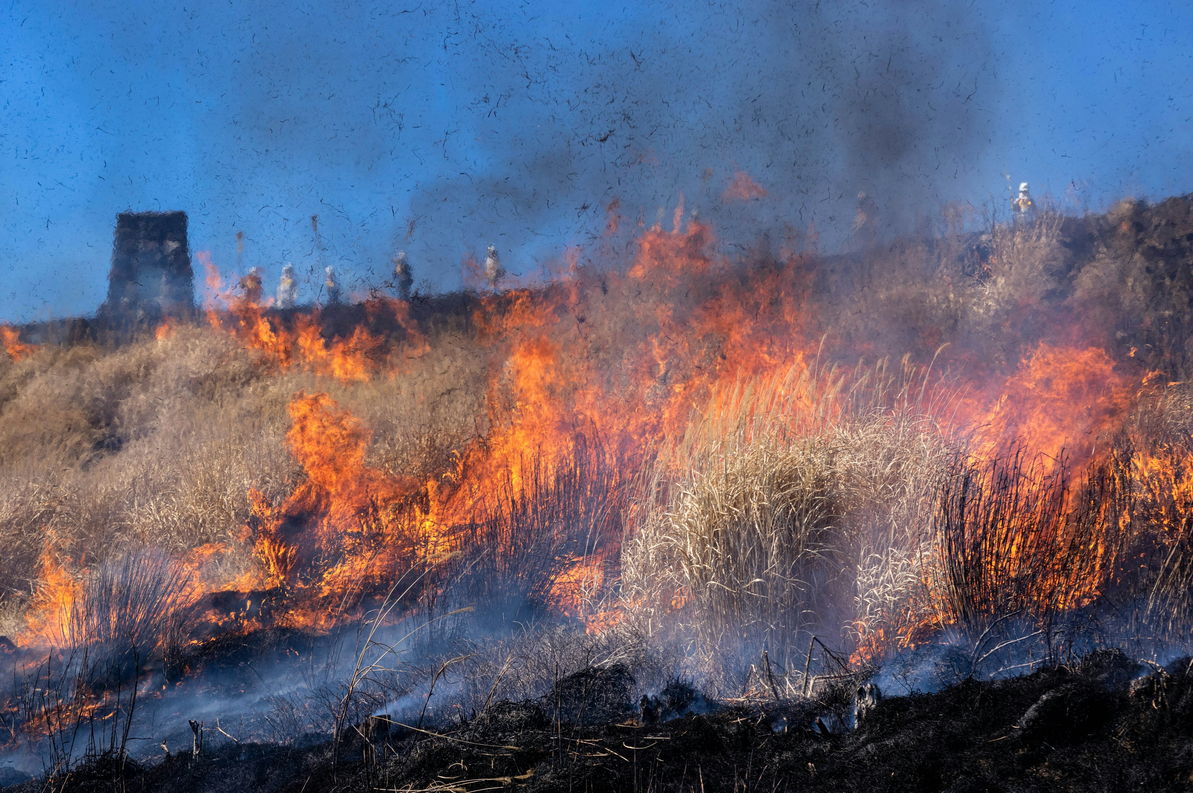 Burning grassland with flames and smoke firefighters attempting to extinguish the fire