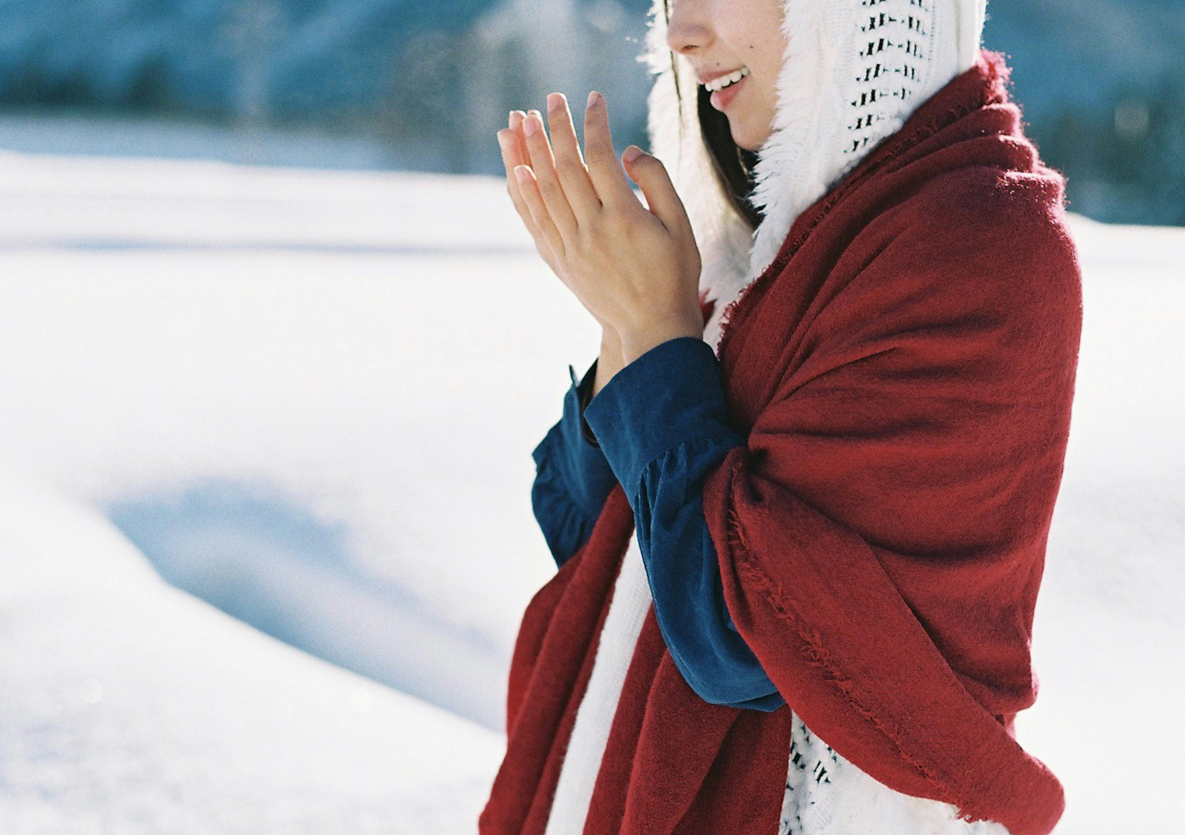 Portrait of a woman in snow with hands together wearing a red shawl and a serene expression