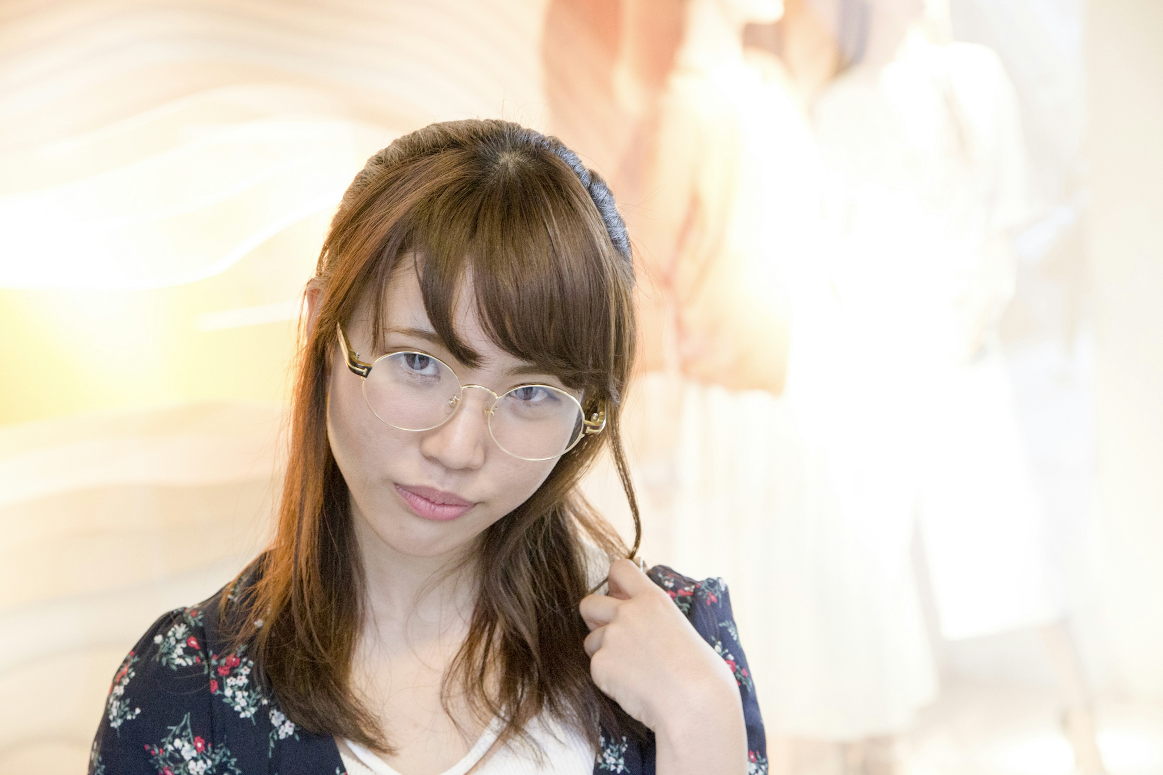 Une jeune femme portant des lunettes pose avec une expression sérieuse affichage de vêtements flou en arrière-plan