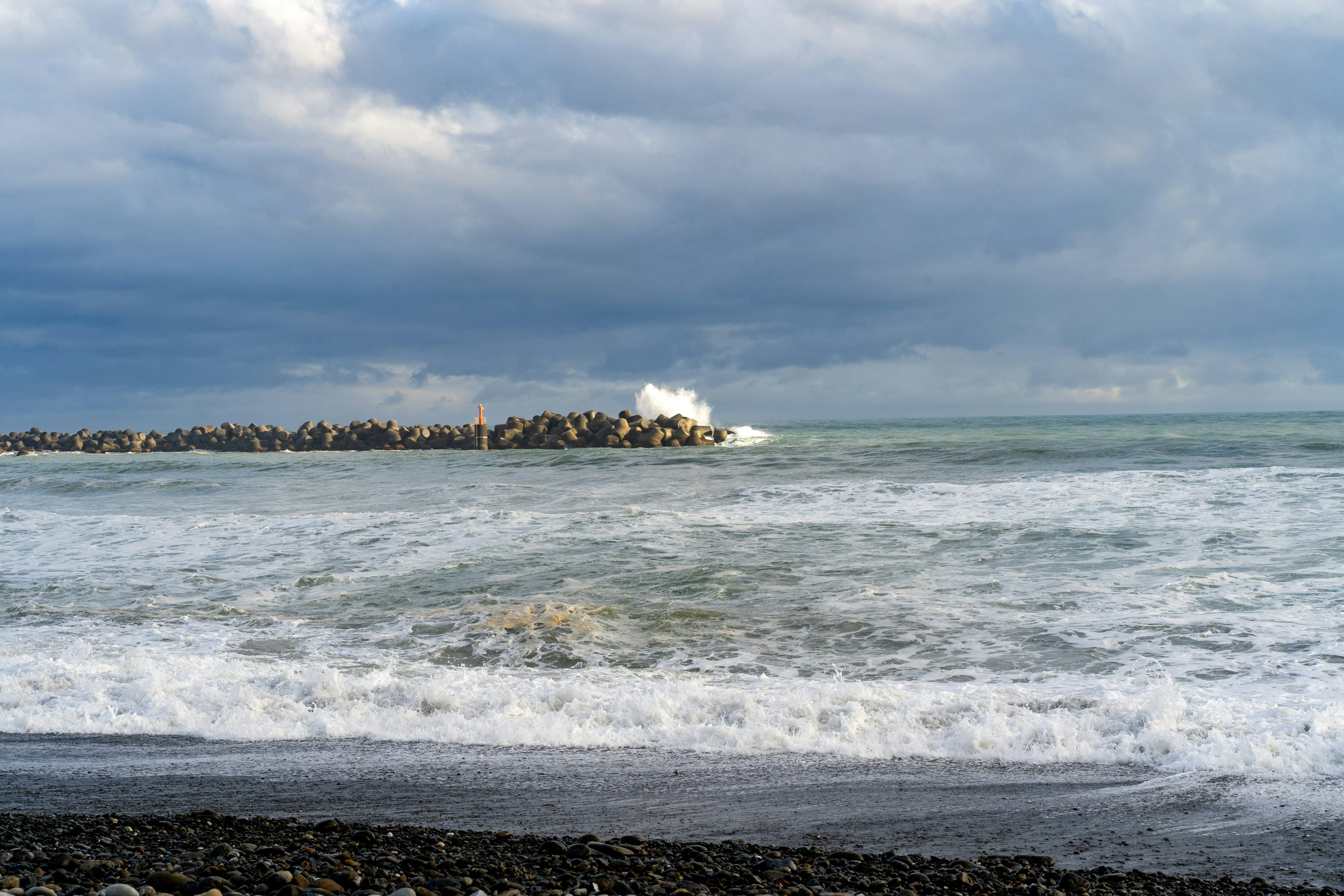 Vista costera con olas rompiendo y un rompeolas de rocas