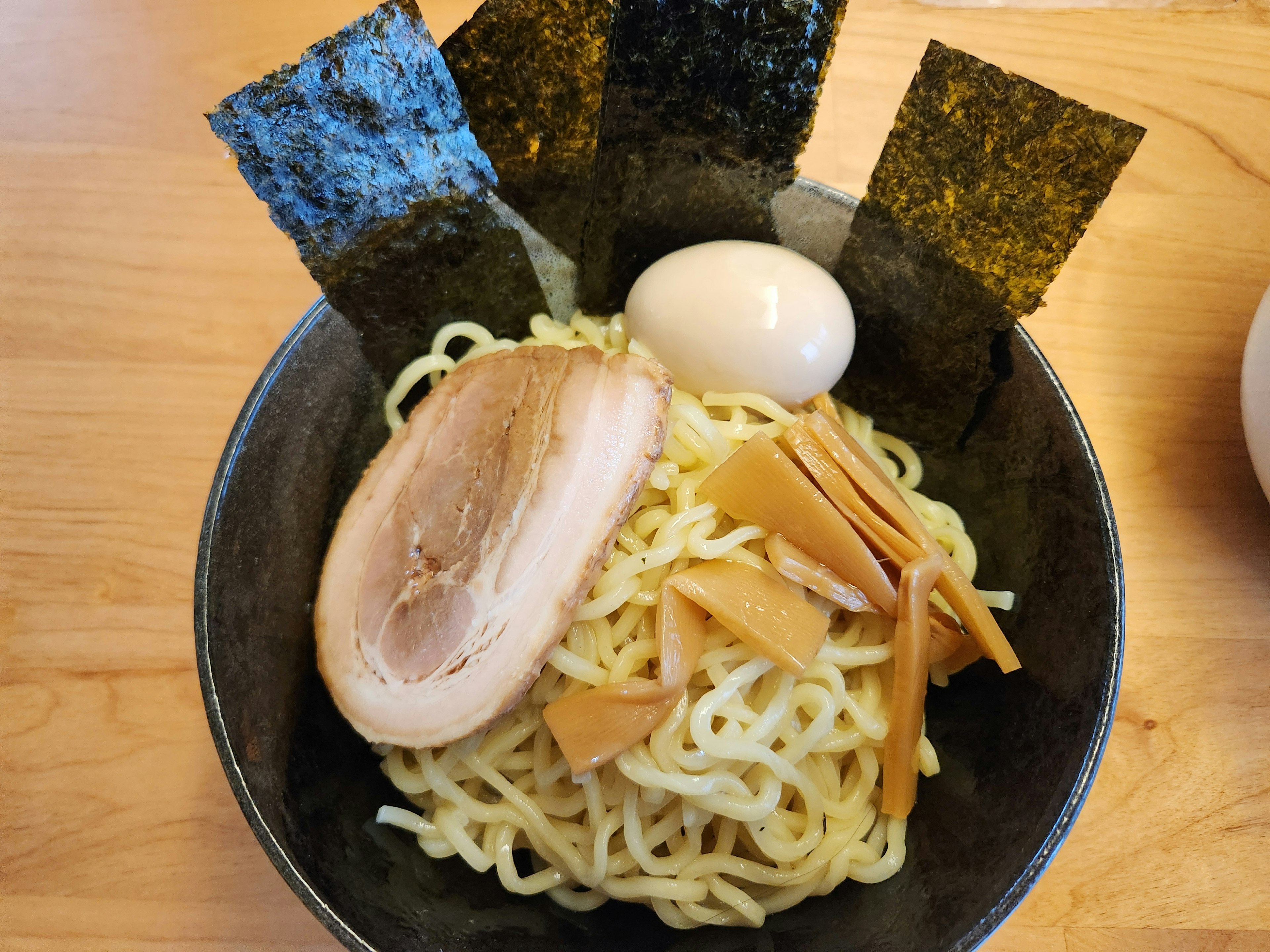 ラーメンのボウルに入った細い麺とチャーシュー 煮卵、メンマ、海苔のトッピング