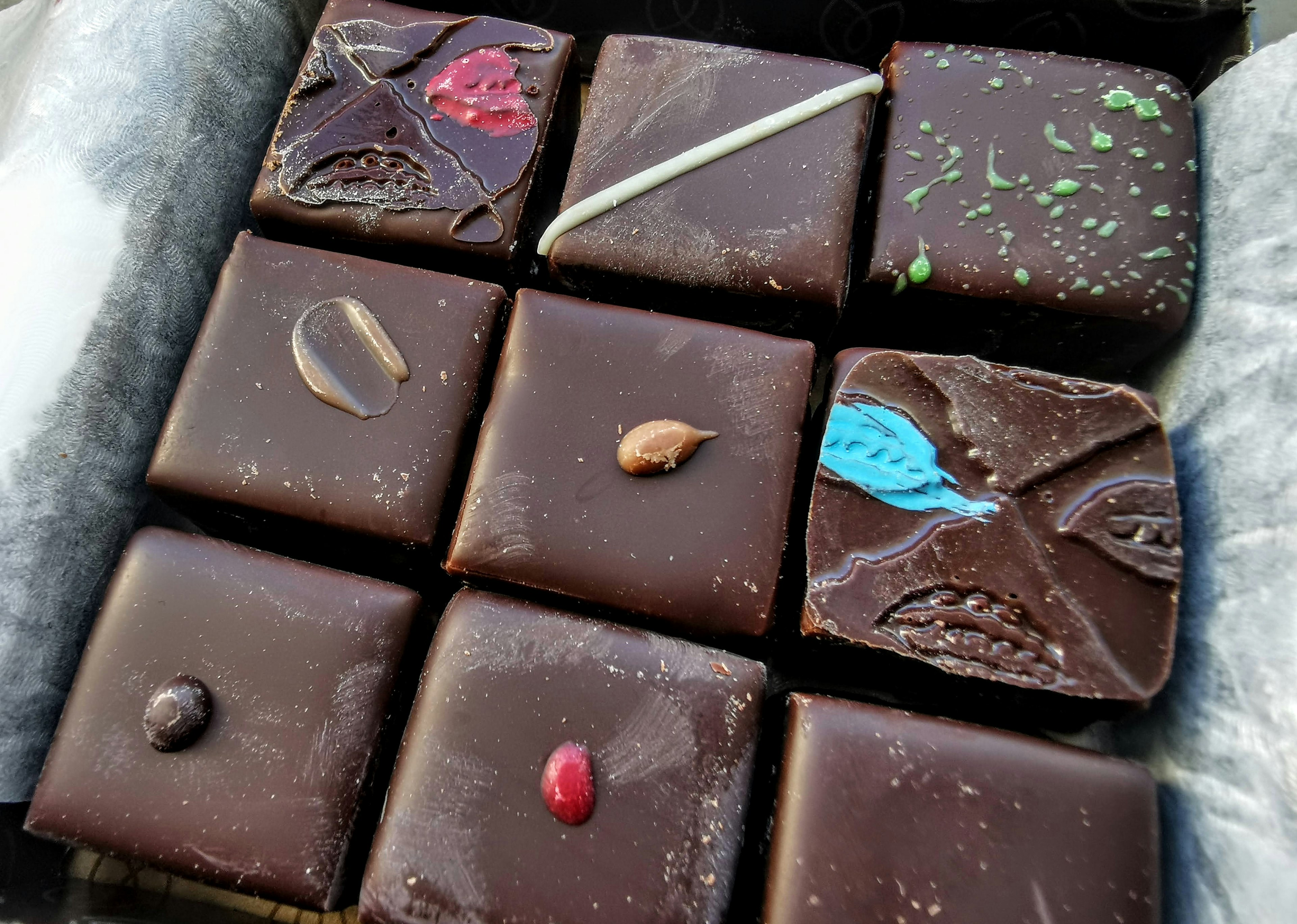 A box of assorted chocolates with colorful toppings on dark chocolate squares