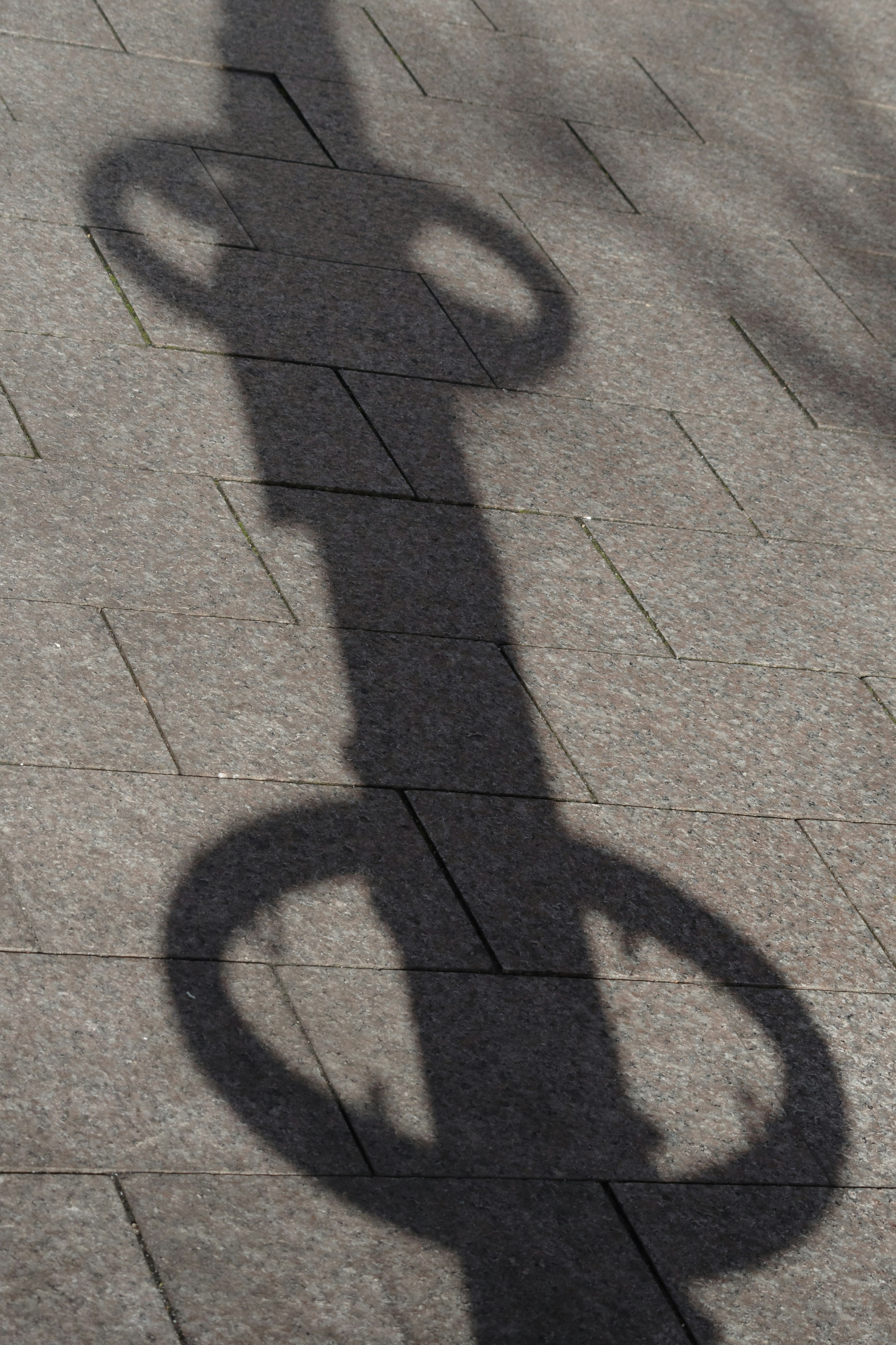 Shadow of a pole with circular elements on pavement