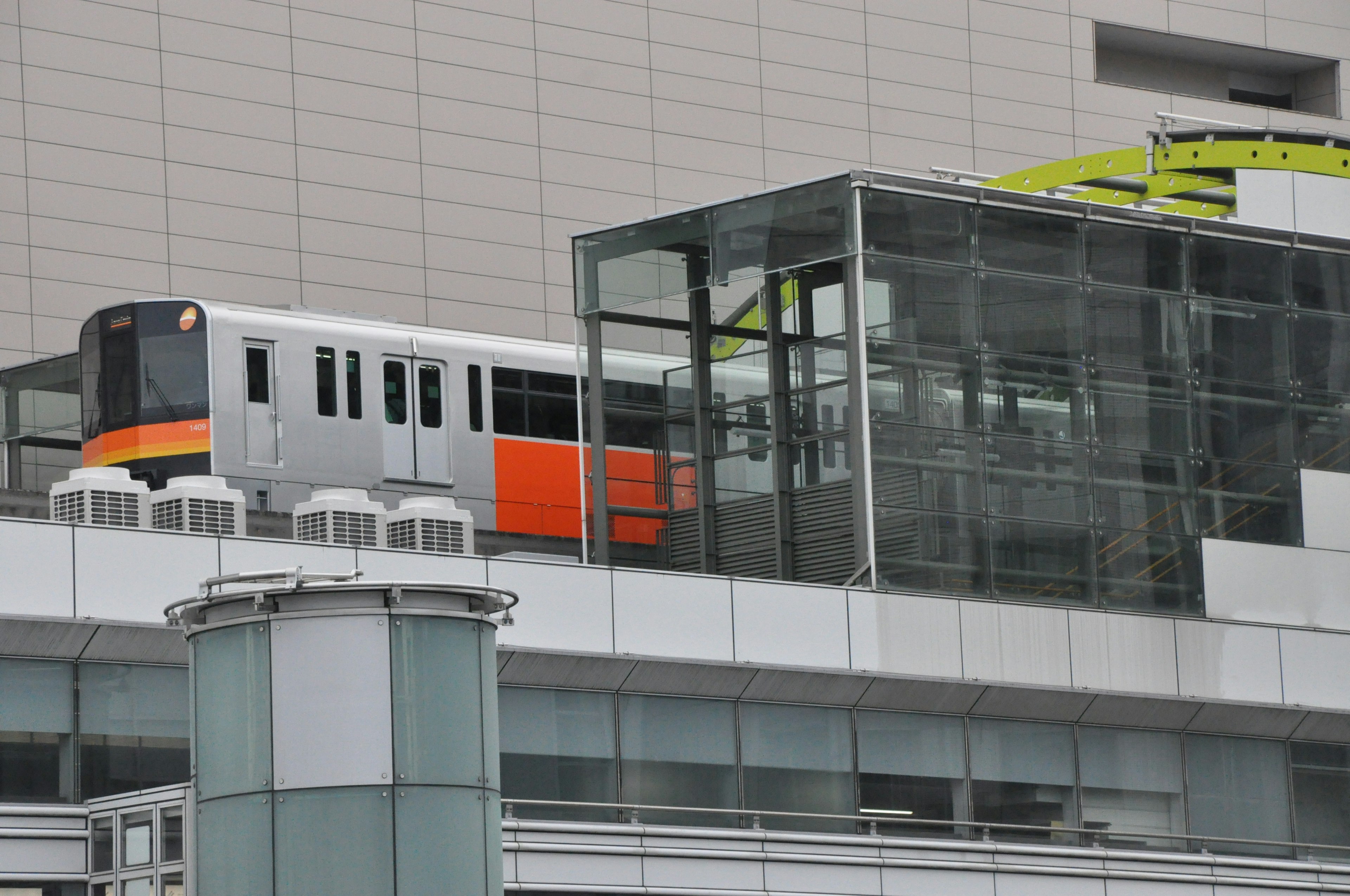 ガラスの構造物の上に停車中のオレンジと銀色の電車