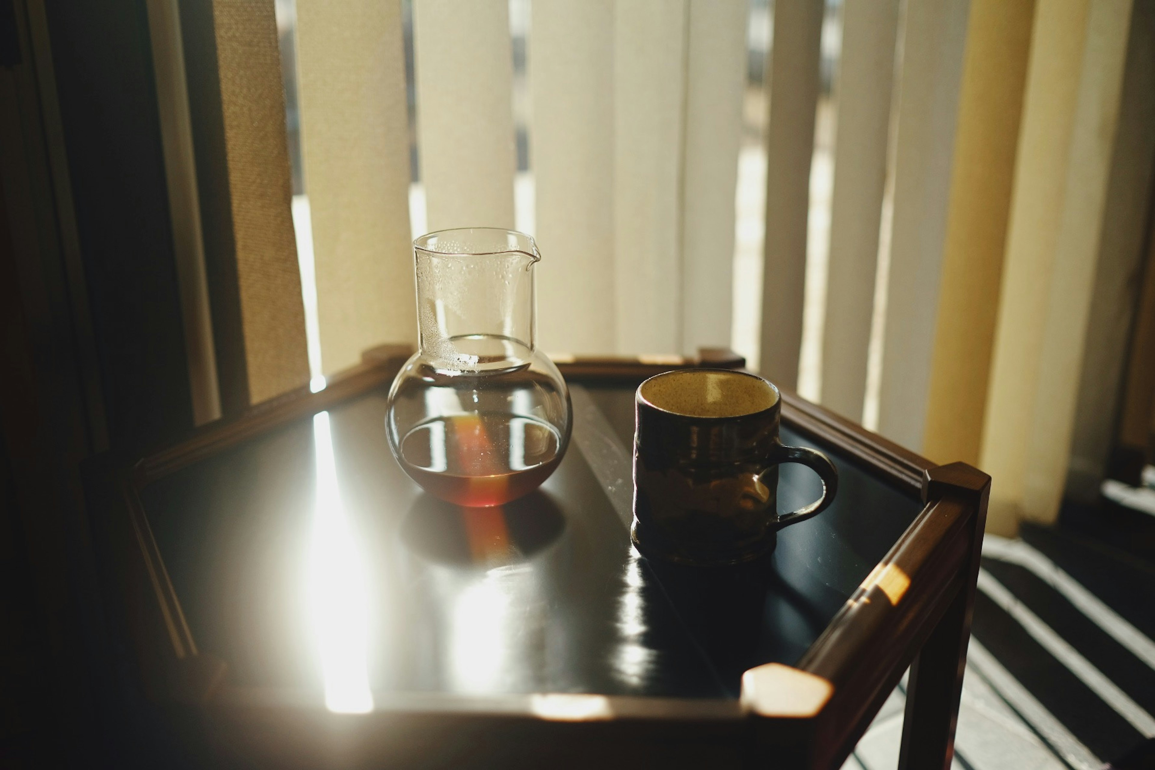 A glass pitcher and a mug on a table with sunlight reflecting off the surface