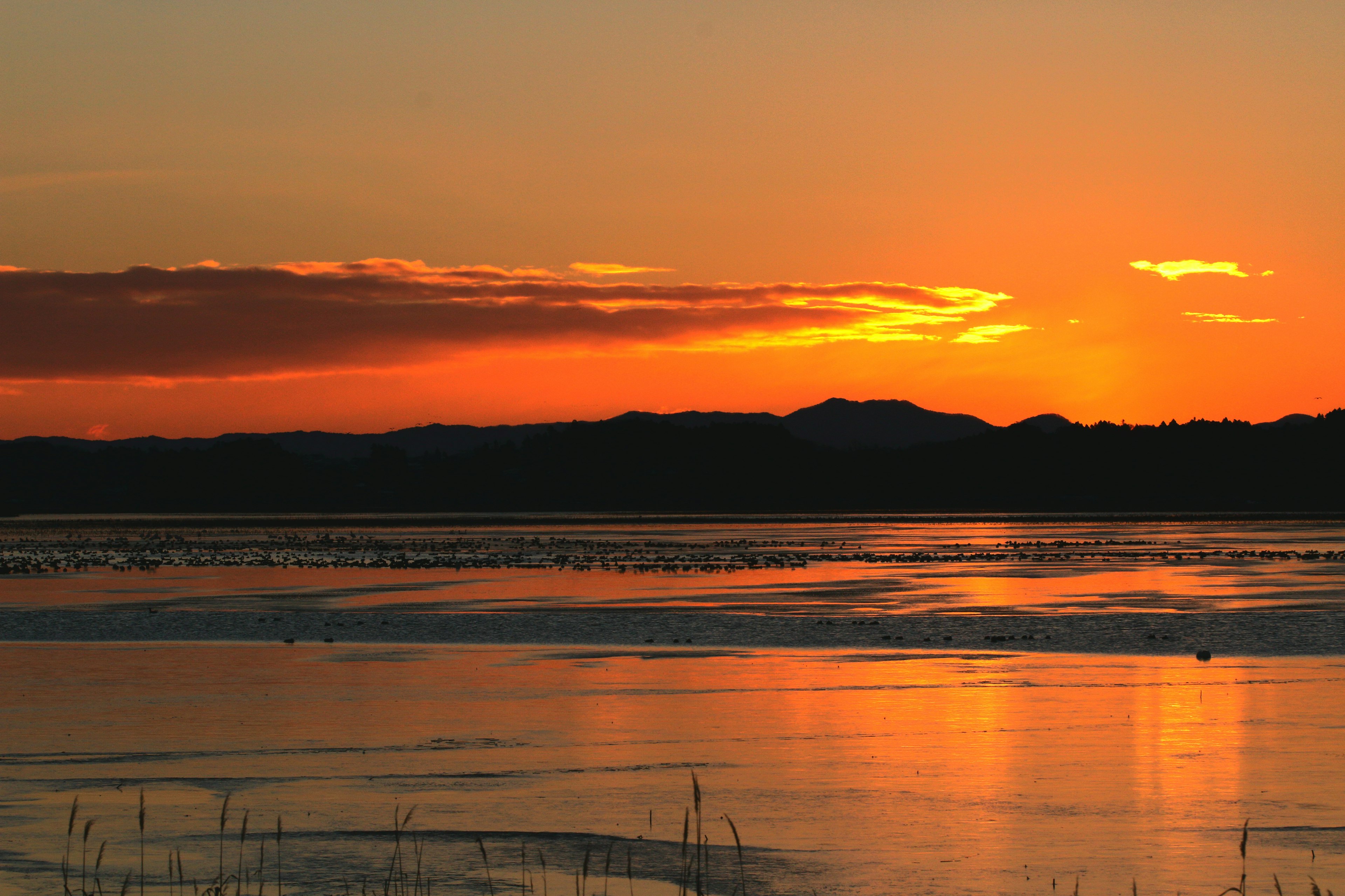 Bellissimo tramonto su un lago con silhouette di montagne e riflessi sull'acqua