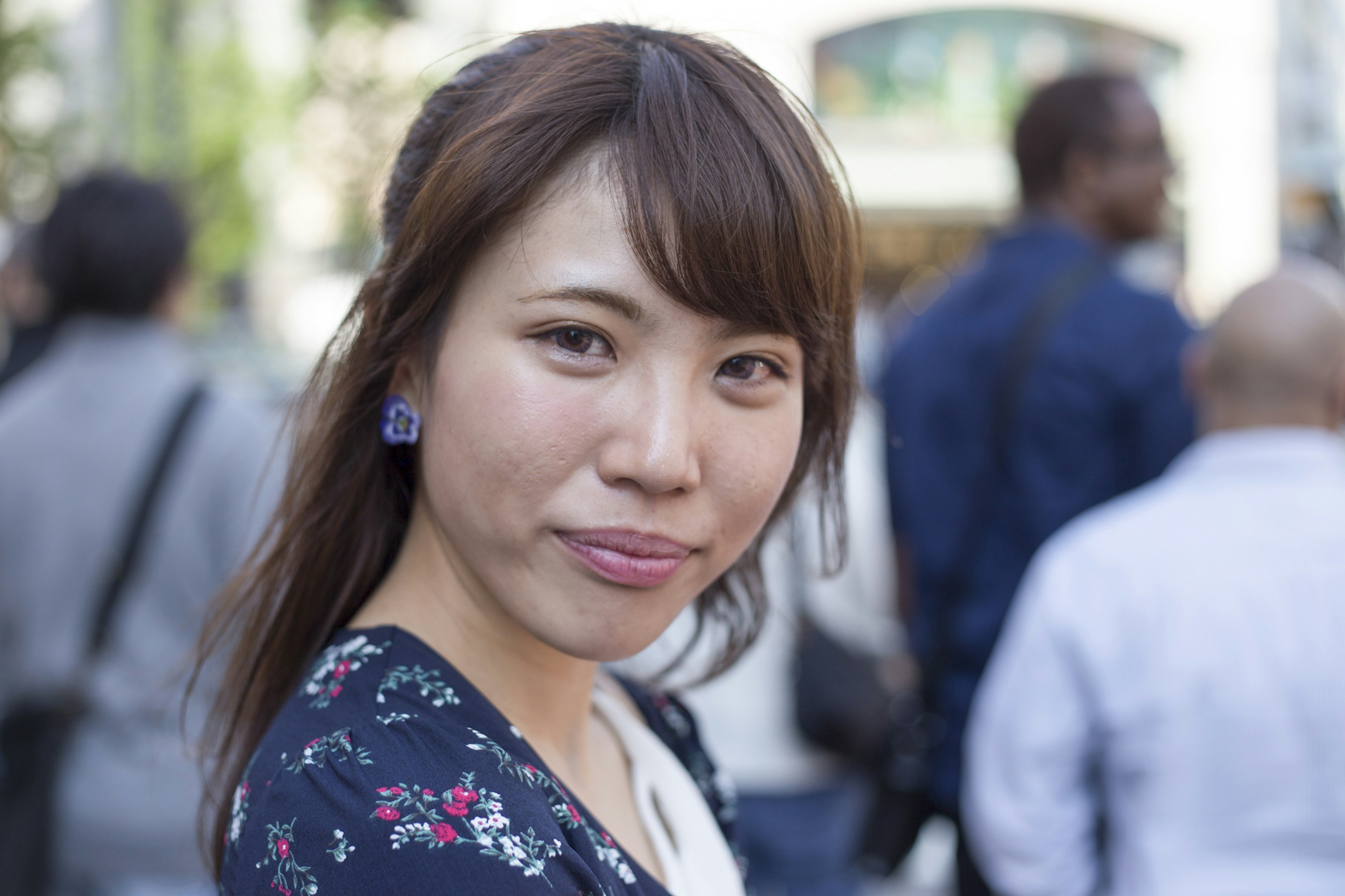 A woman smiling in a floral dress outdoors in a bustling street