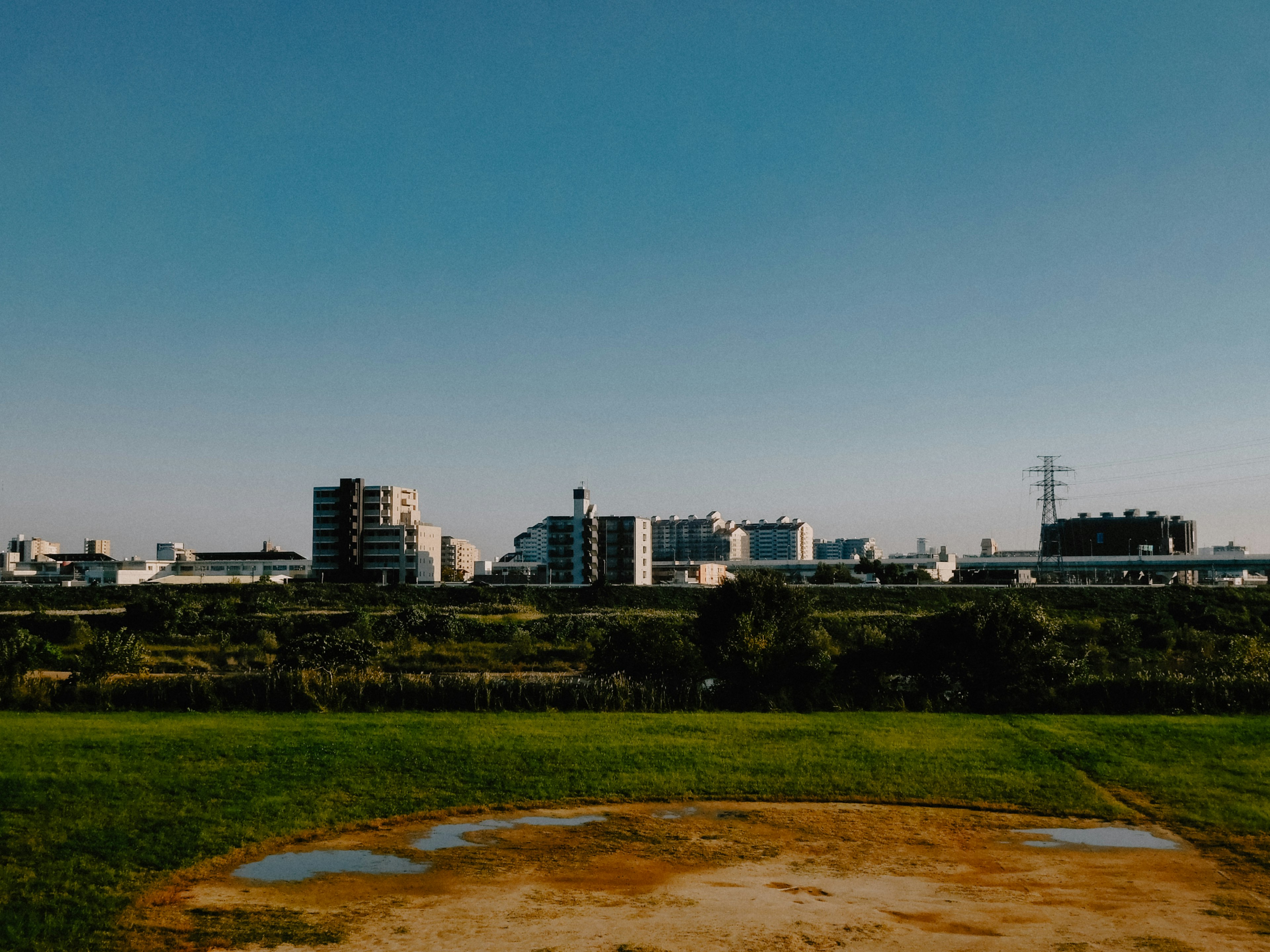 Urban skyline under a clear blue sky with green grass in the foreground