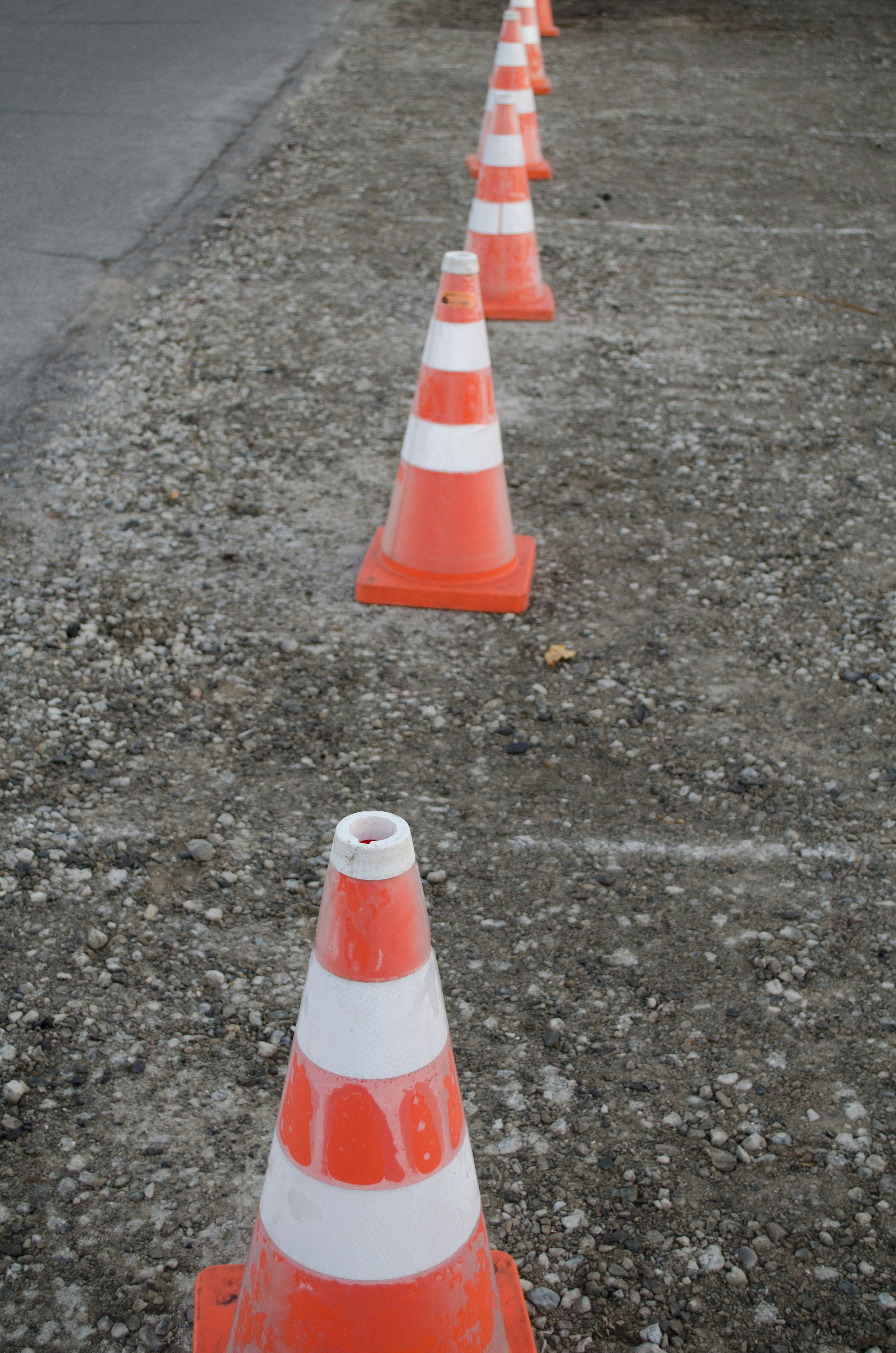 A row of orange and white traffic cones on a gravel surface