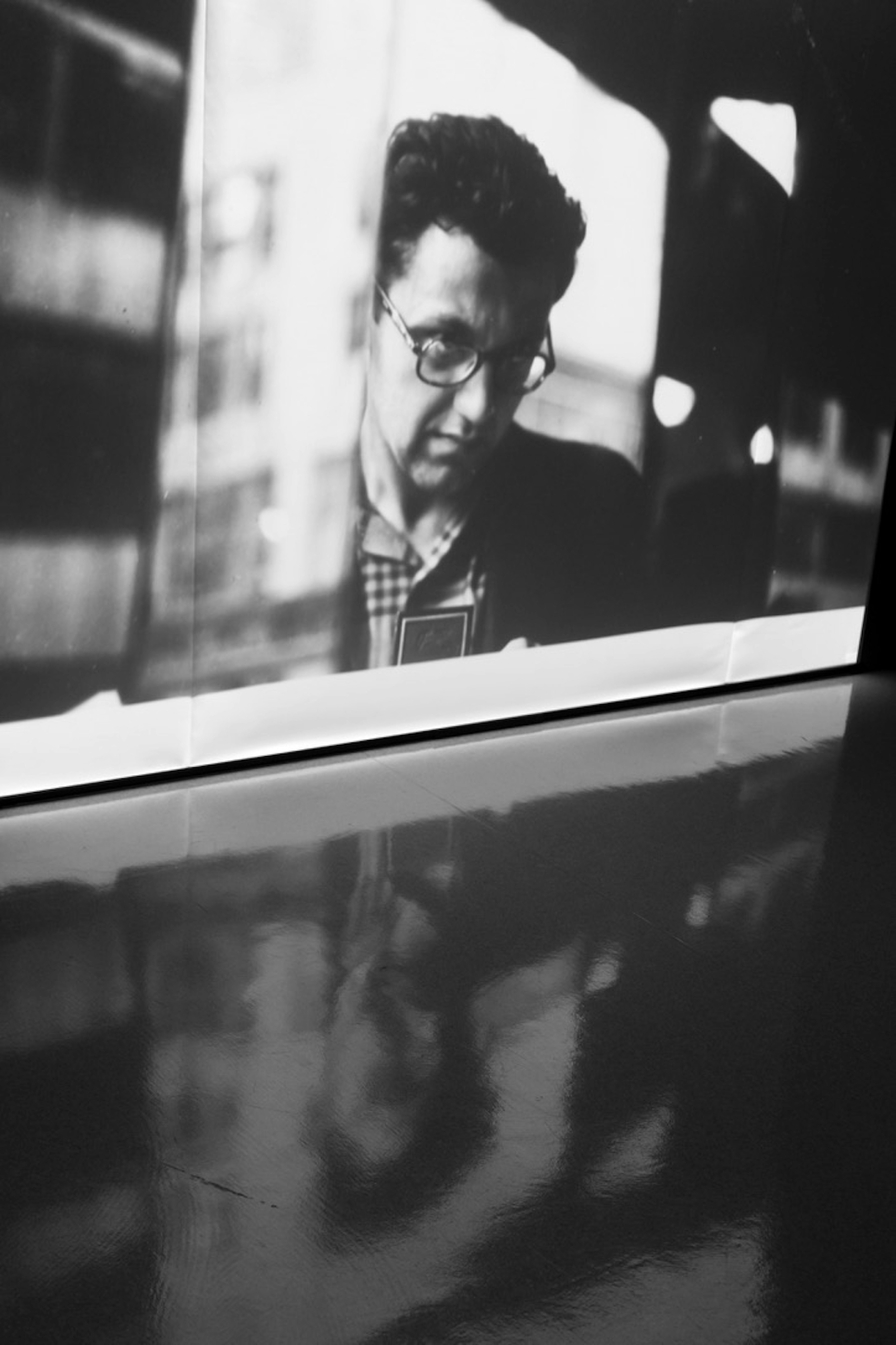 Black and white photograph of a man looking down with a focused expression reflections visible in the glass