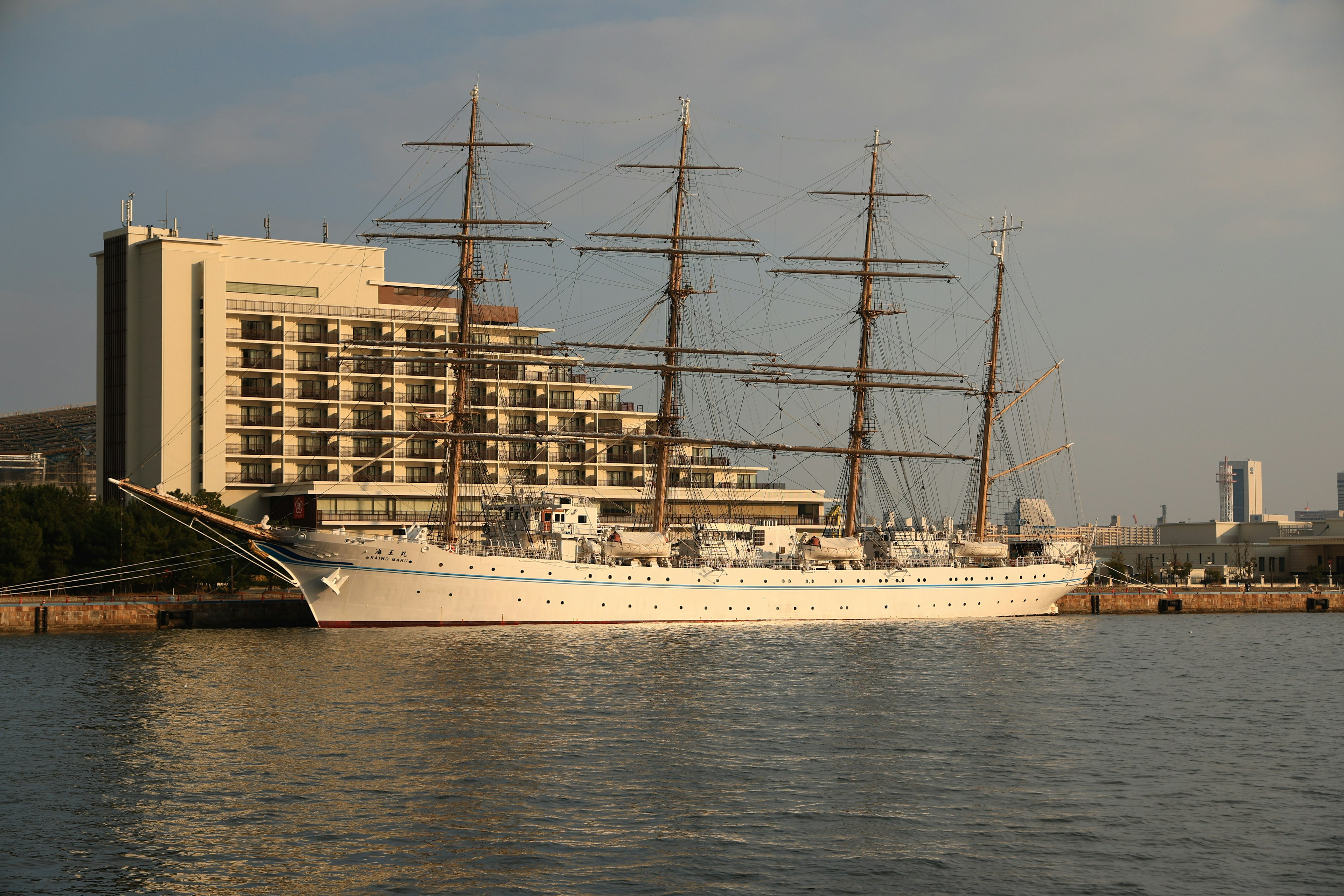 A beautiful sailing ship docked at the harbor with a modern building behind it