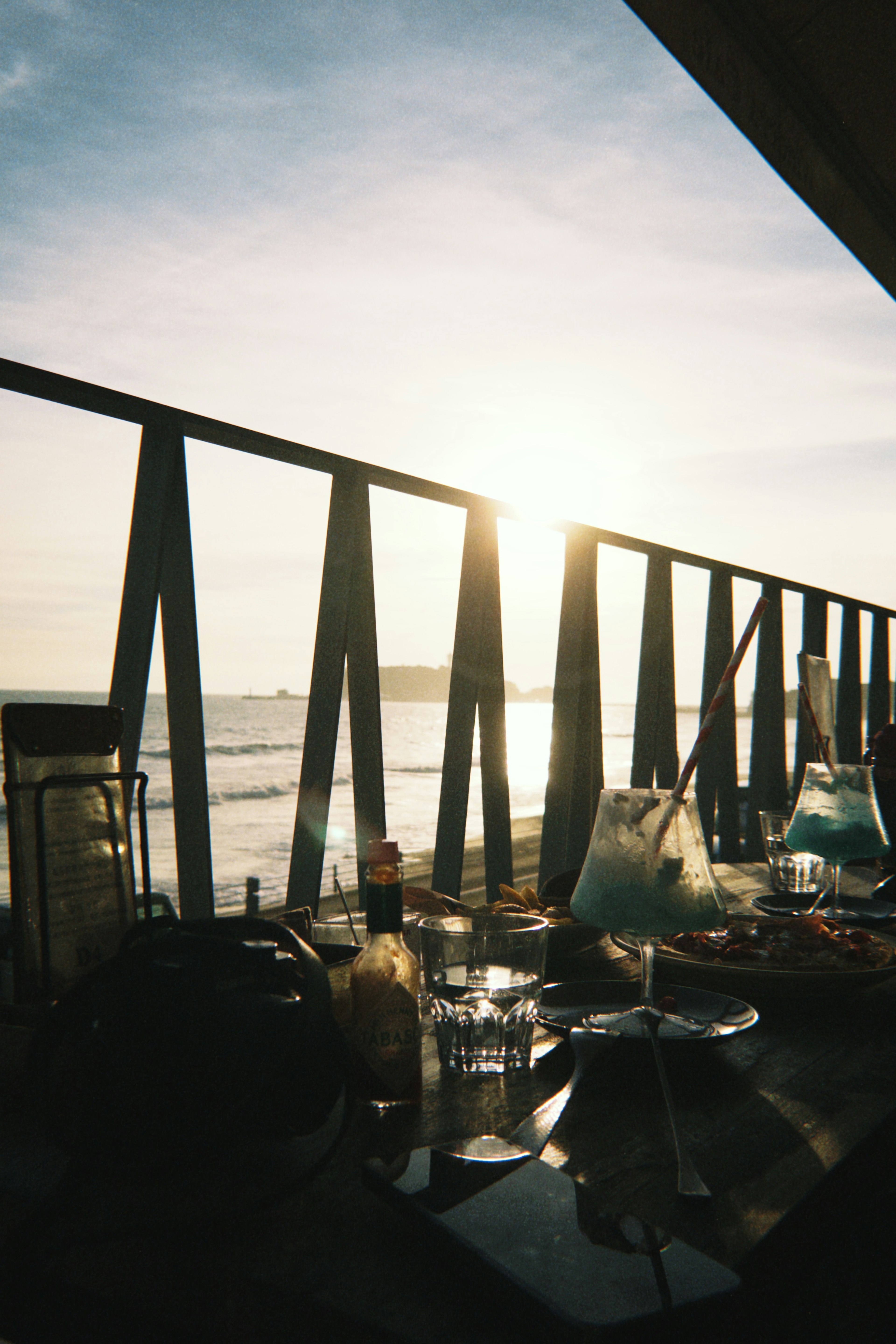 Un bellissimo tramonto sul mare catturato da un balcone con una ringhiera e bicchieri sul tavolo