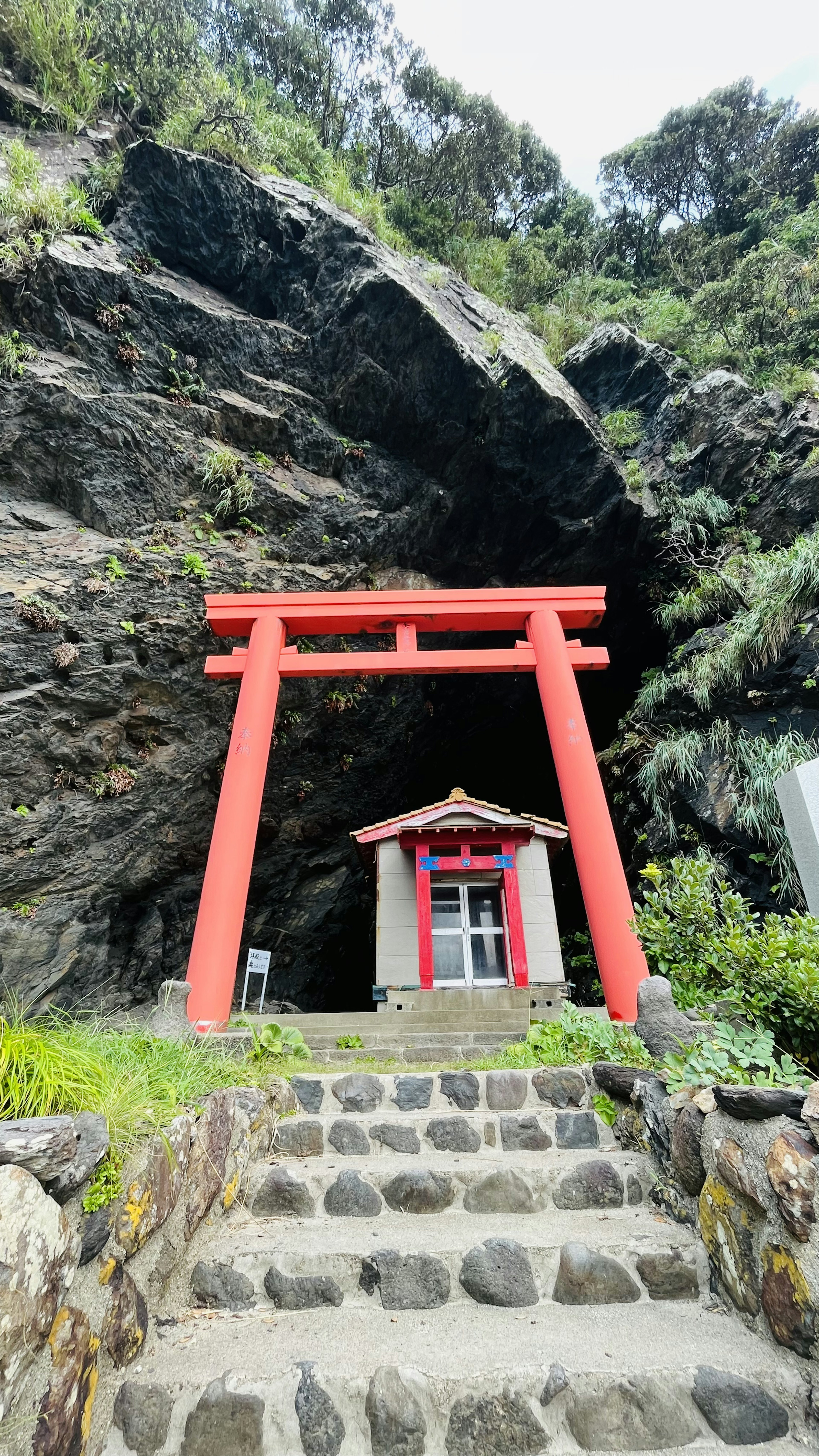 Portale torii rosso e piccolo santuario all'ingresso di una grotta rocciosa