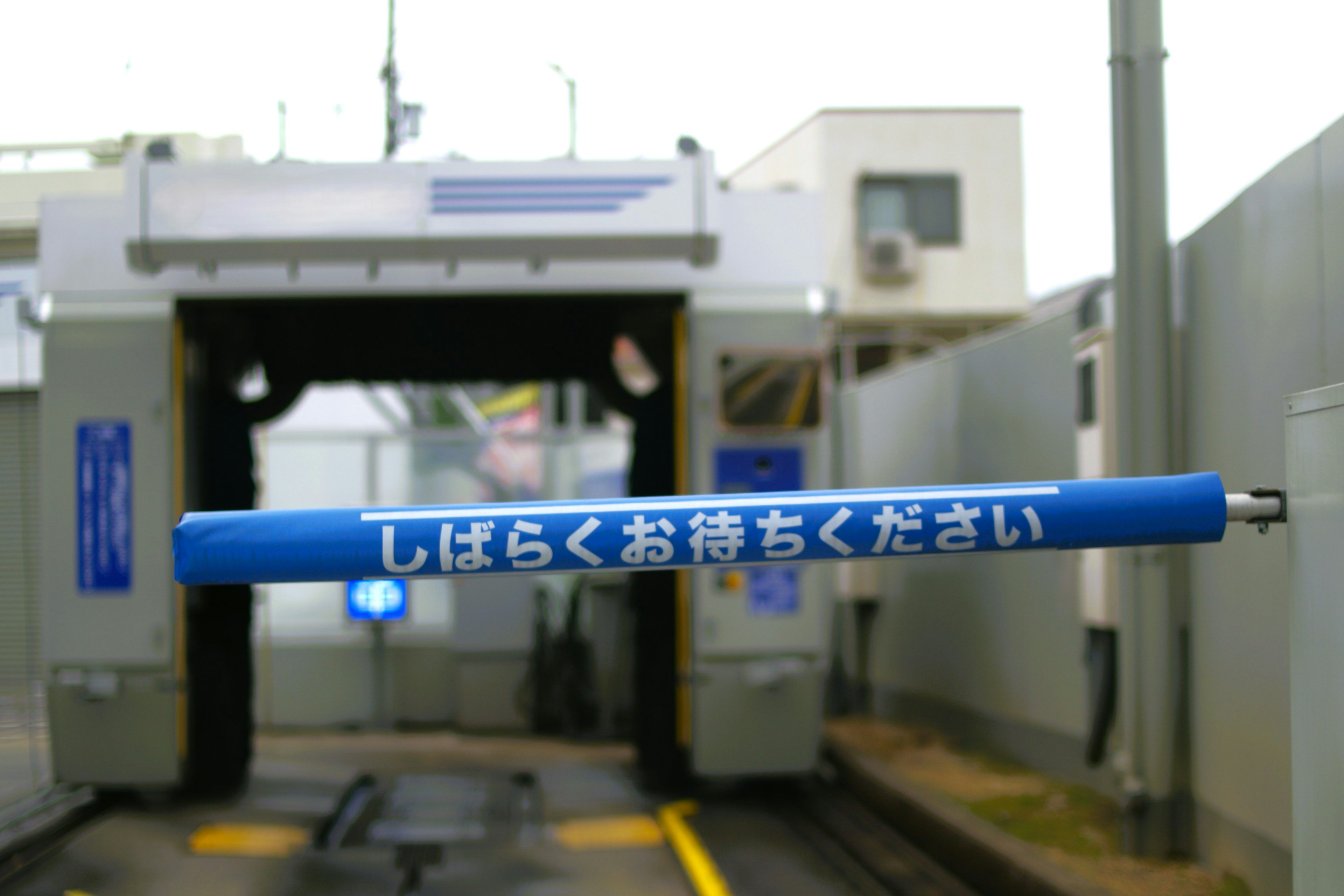 Blue barrier bar at a car wash entrance with Japanese instructions above