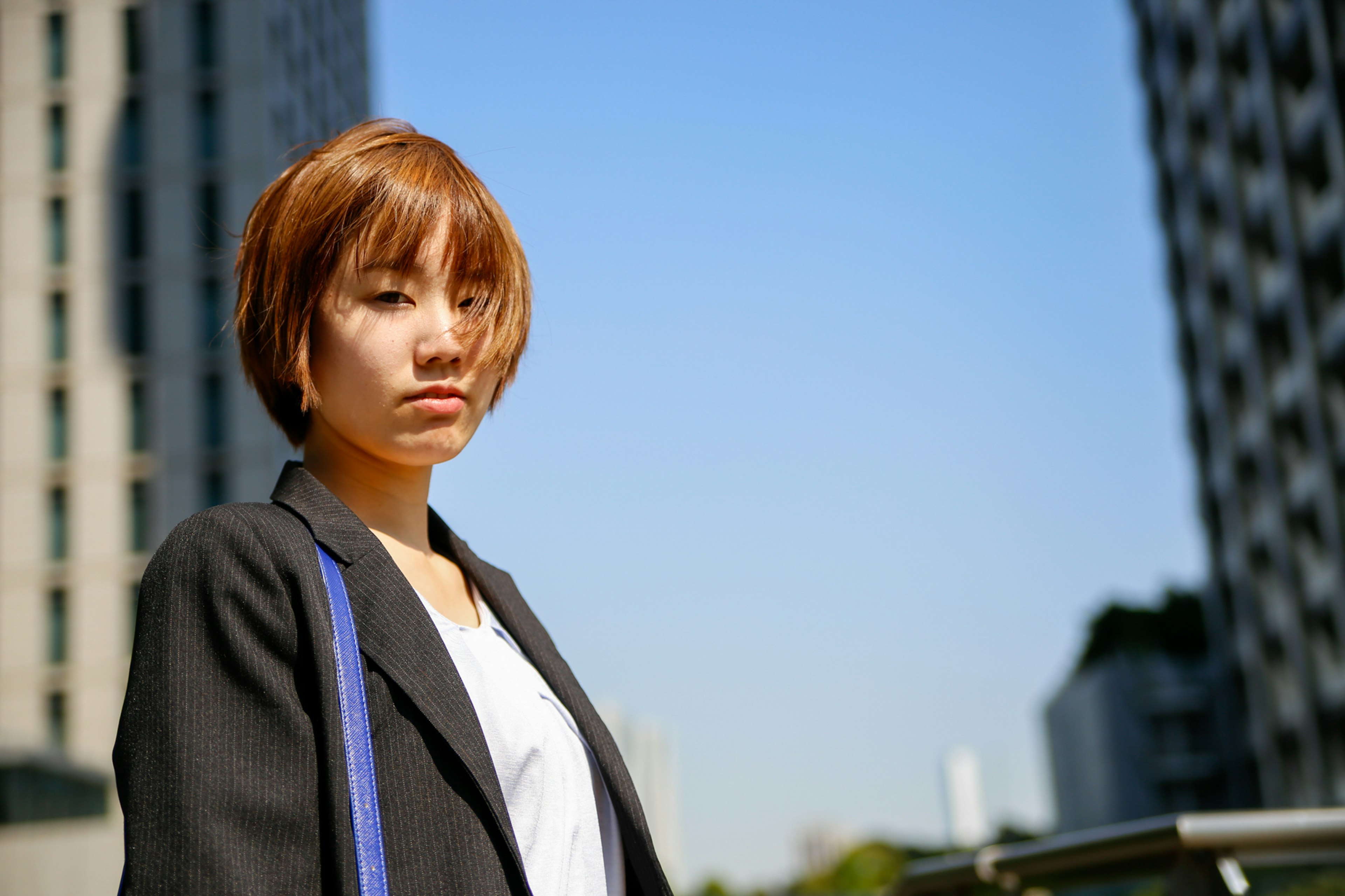 A serious-looking woman standing under a blue sky in an urban setting