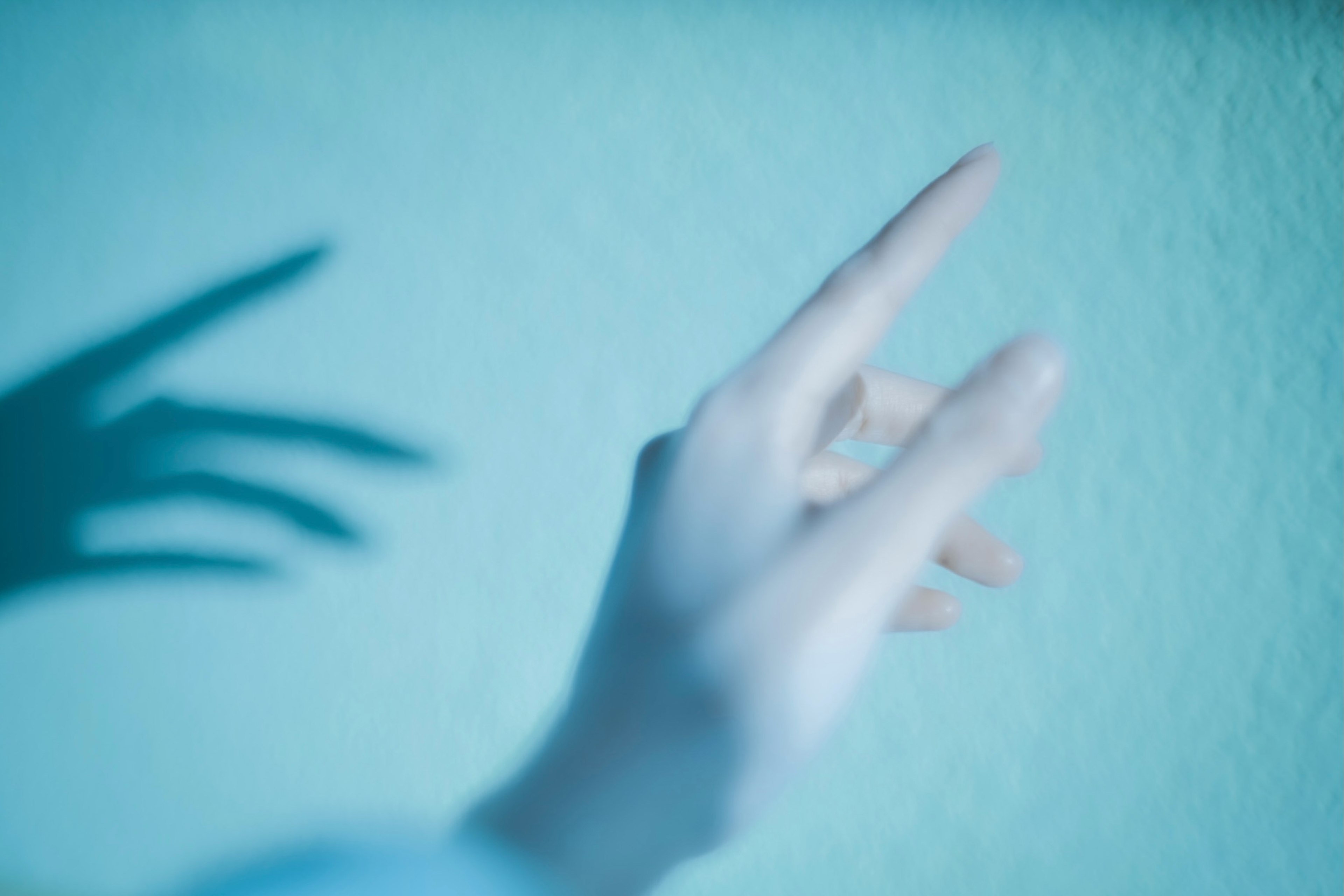 A hand pointing at a blue wall with a shadow cast