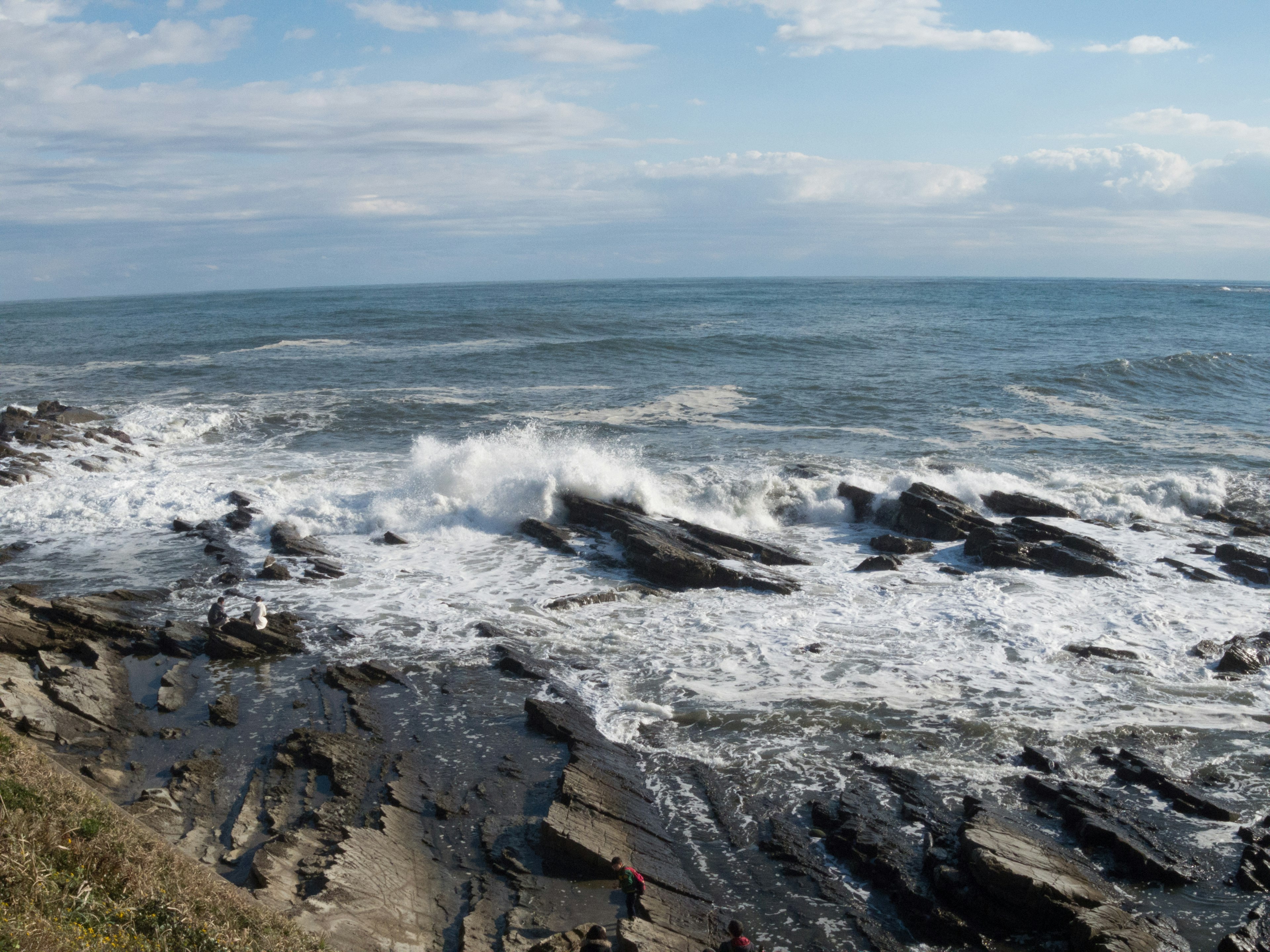 Coastal scene with waves crashing against rocks under a blue sky and clouds