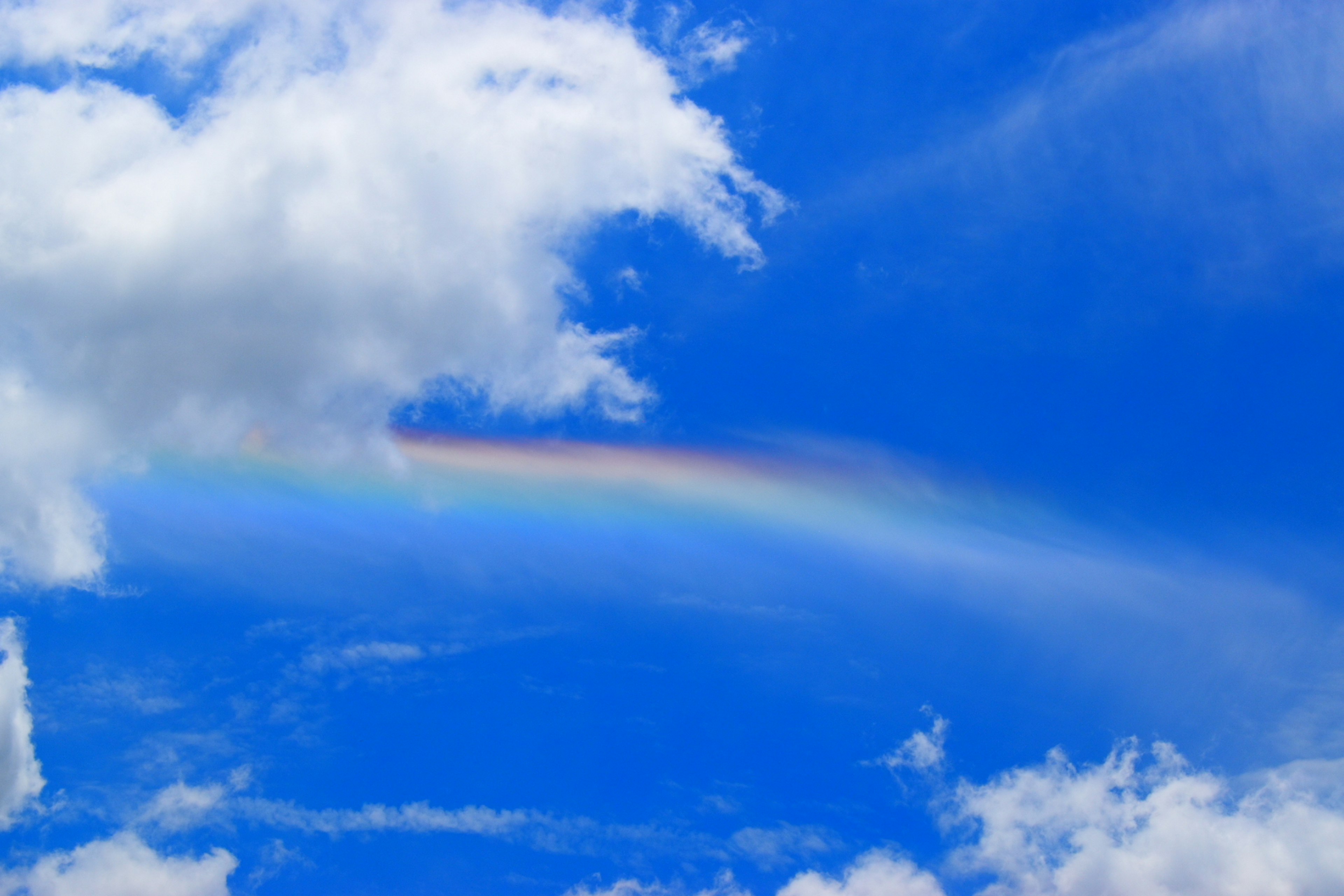 Un arcoíris tenue cruzando un cielo azul brillante con nubes