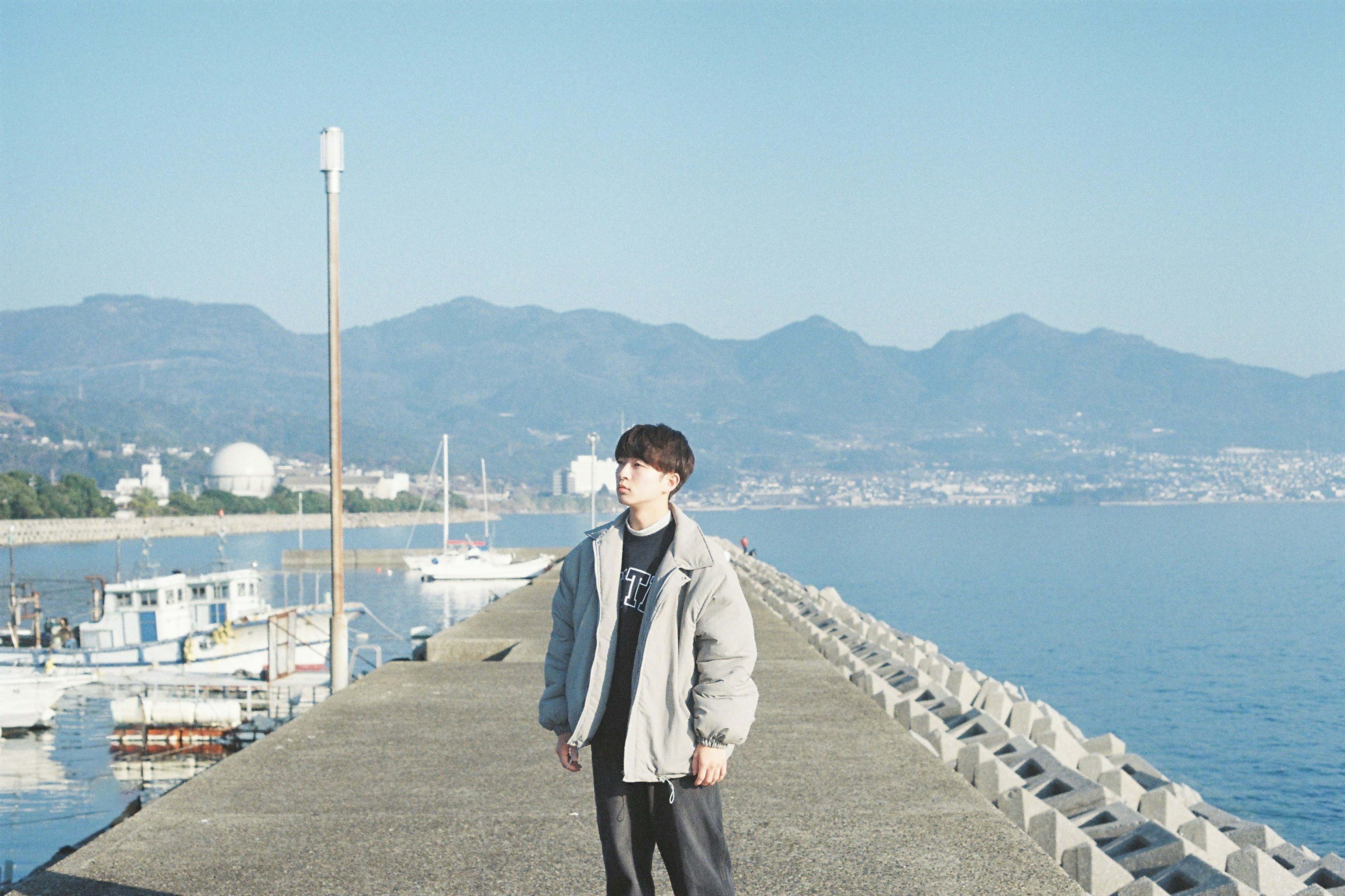 A man standing on a pier with mountains and sea in the background