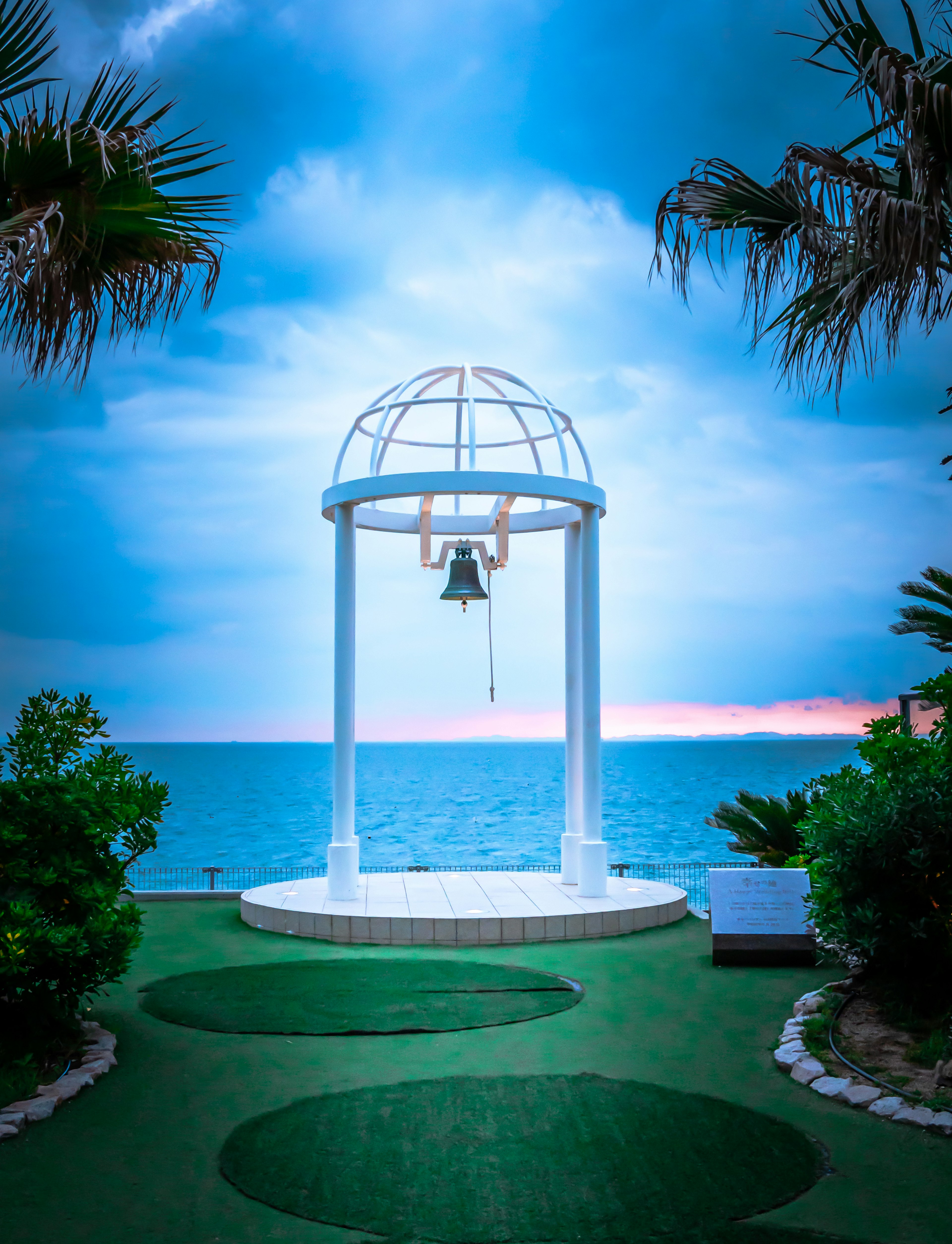 A dome structure with a hanging bell against a beautiful ocean backdrop