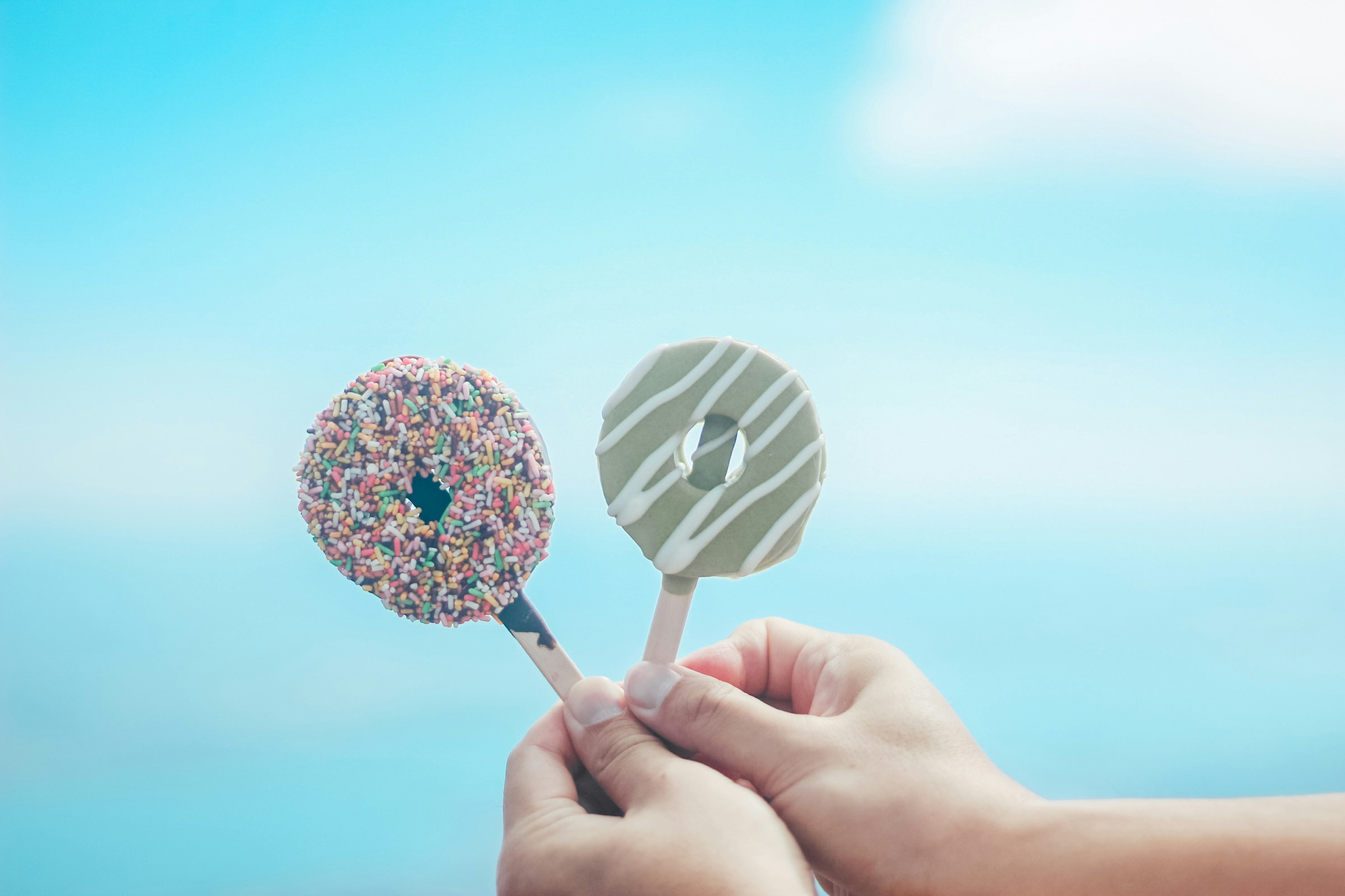 Mani che tengono gelati a forma di ciambella colorati contro un cielo blu