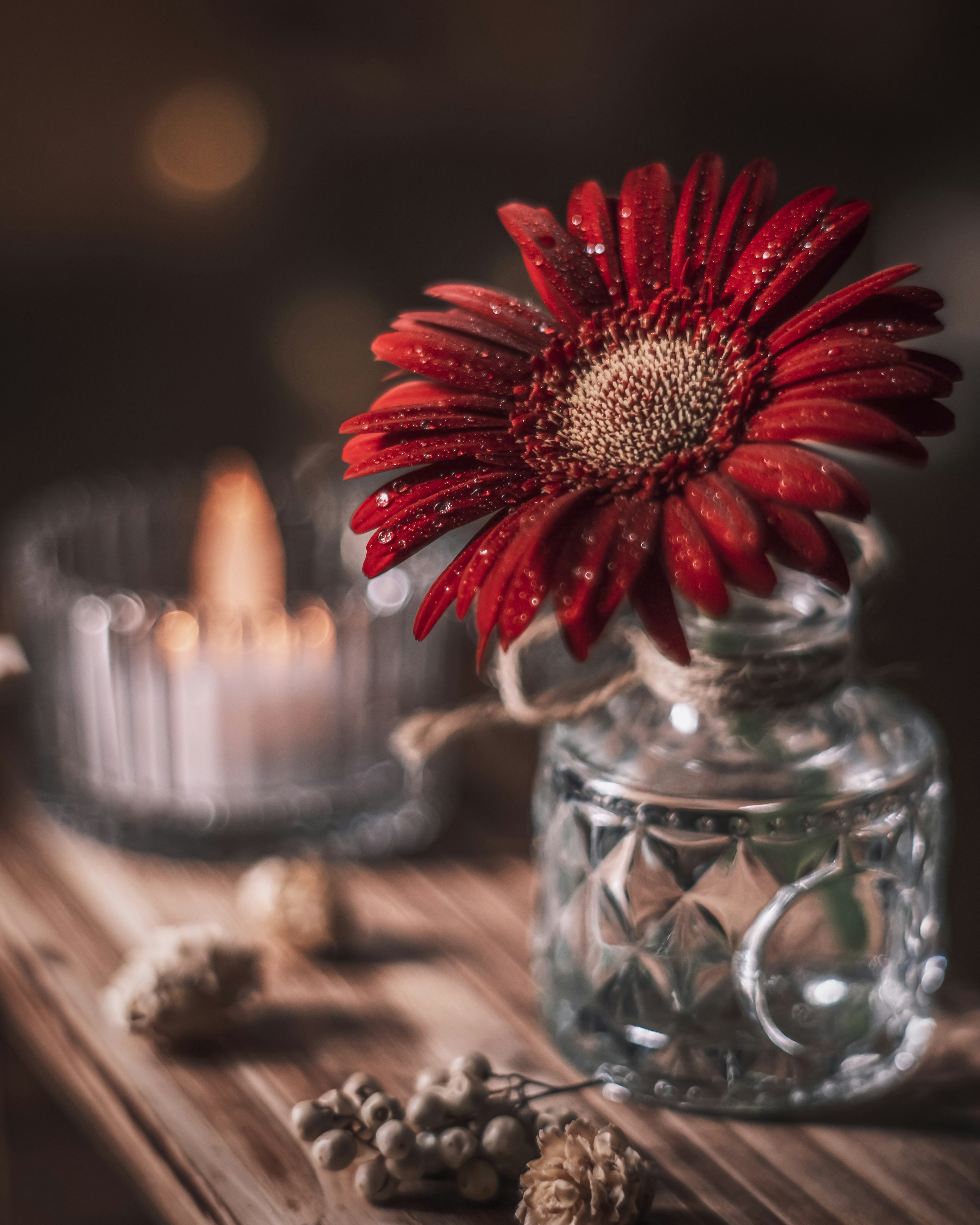 Una flor roja en un jarrón de vidrio transparente con una vela en una mesa de madera