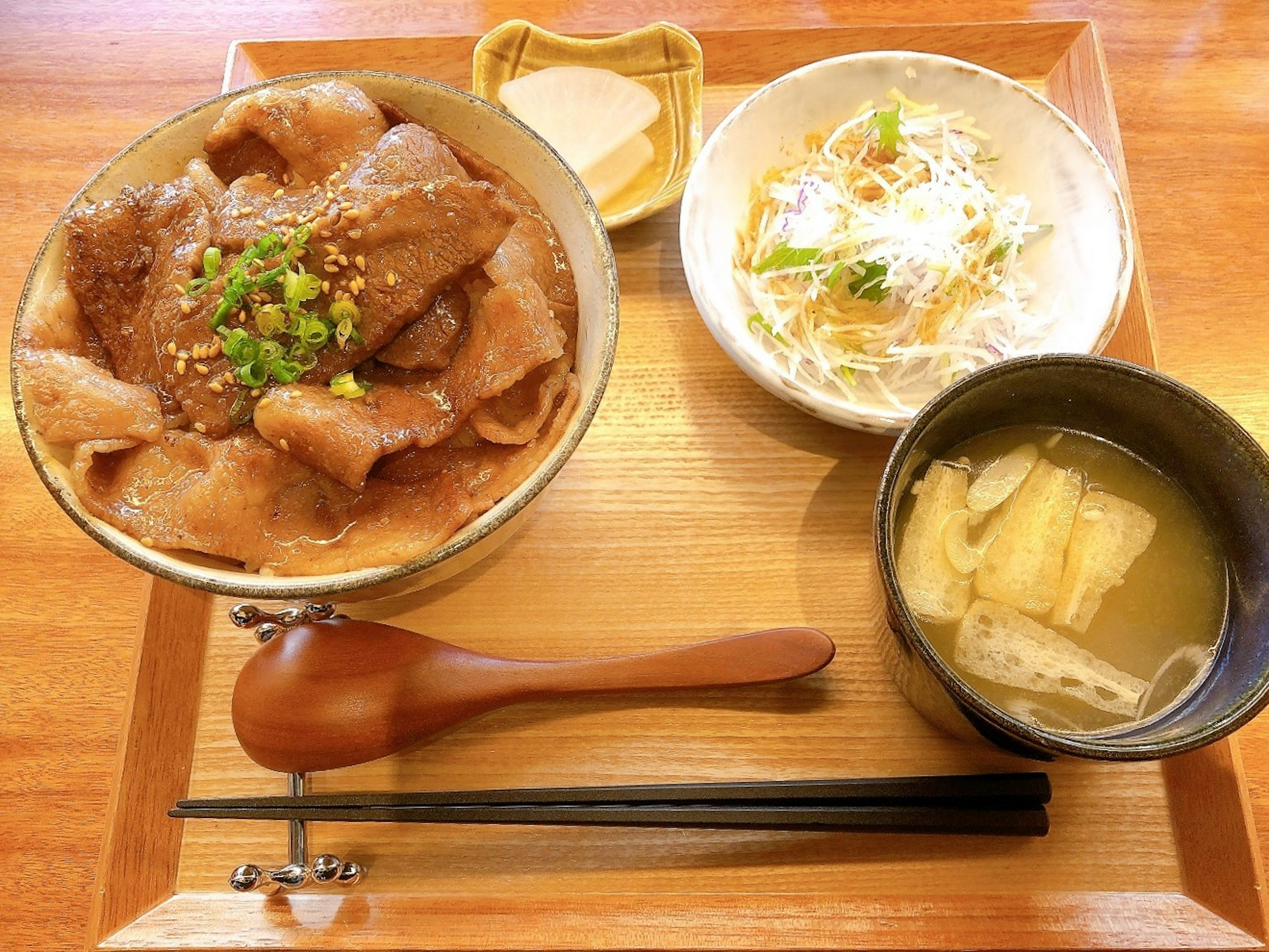 Japanese meal featuring a bowl of pork, salad, and miso soup