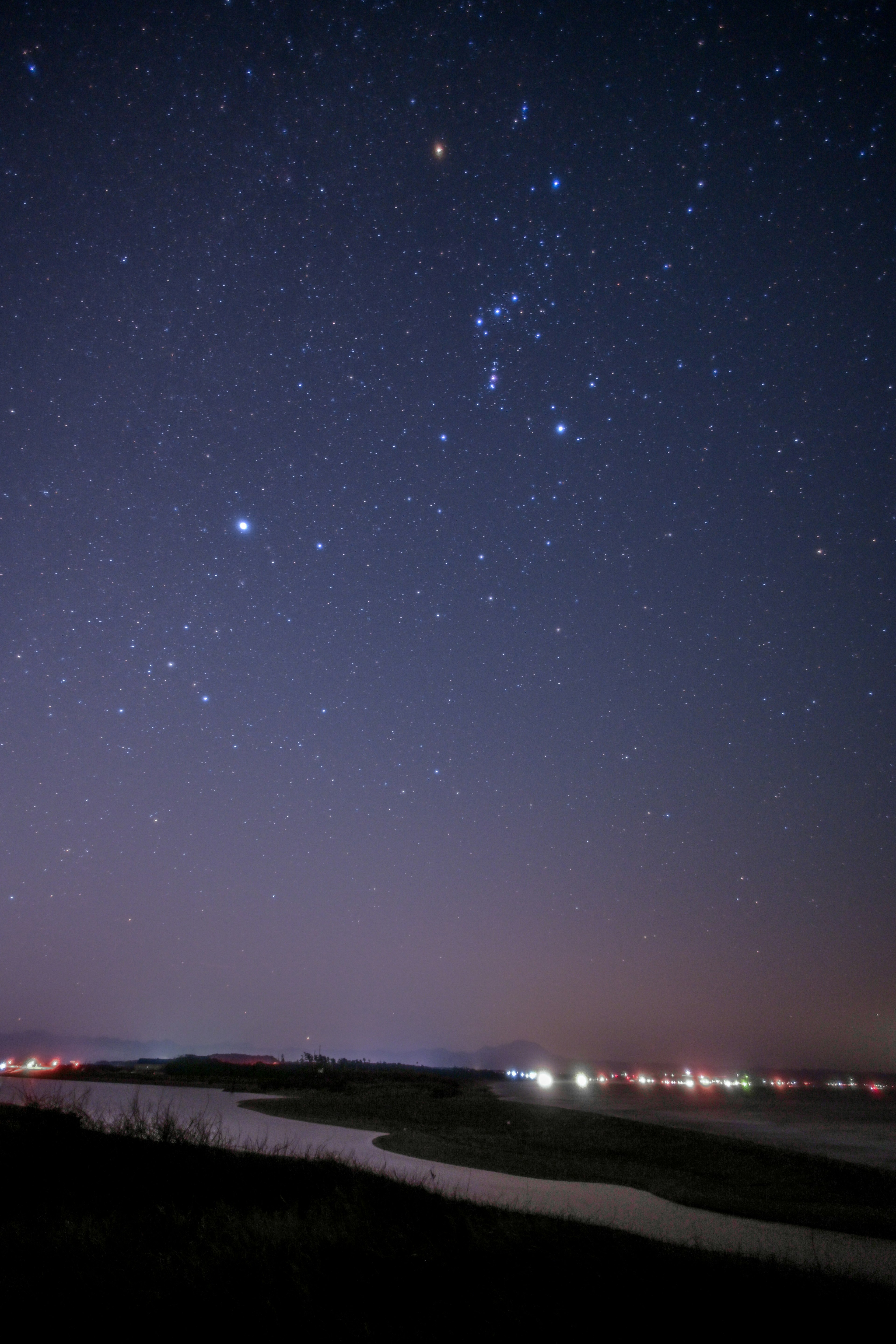 Starry night sky featuring the Orion constellation and a winding river