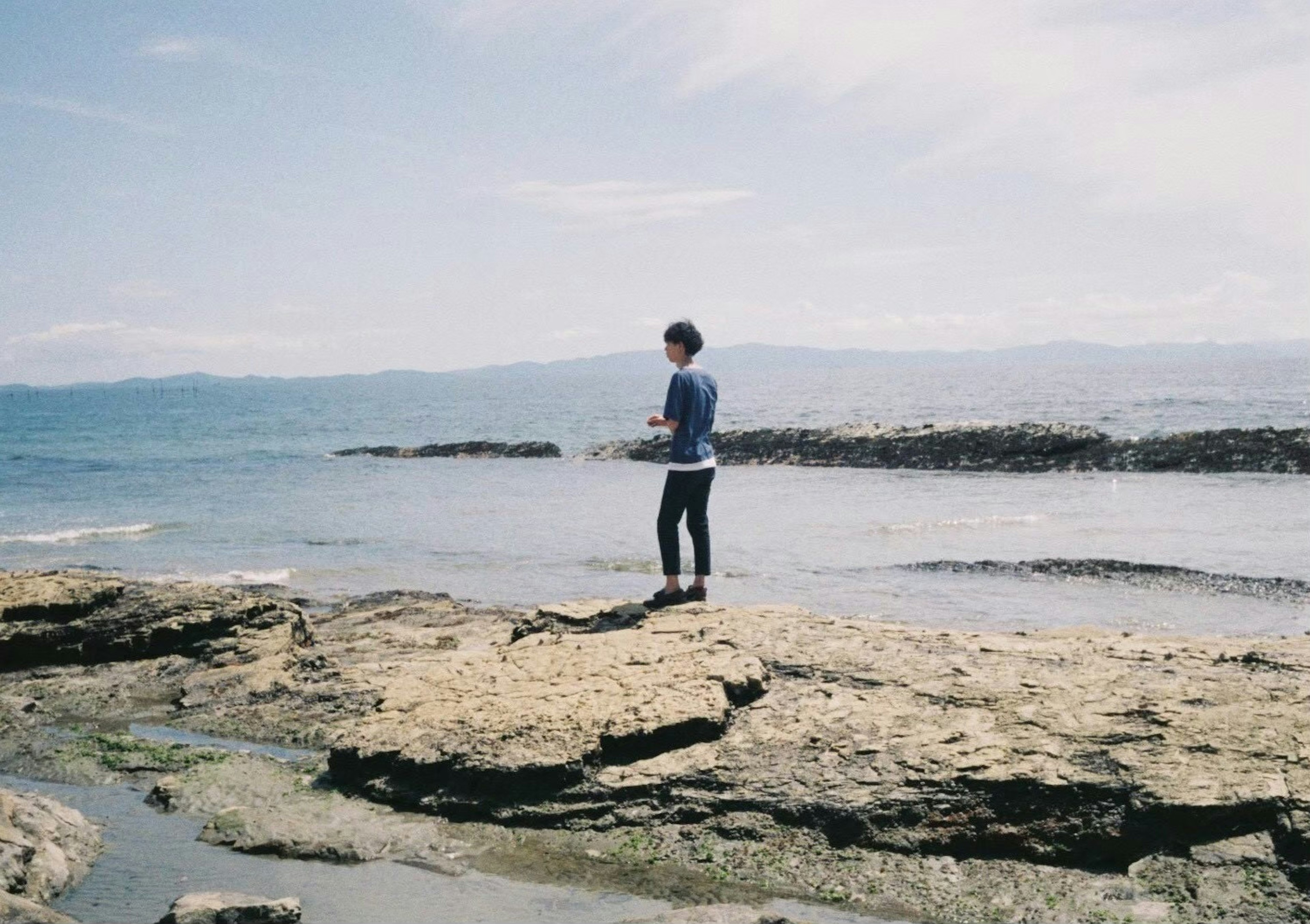 Silhouette of a young person standing on coastal rocks with a wide sea view