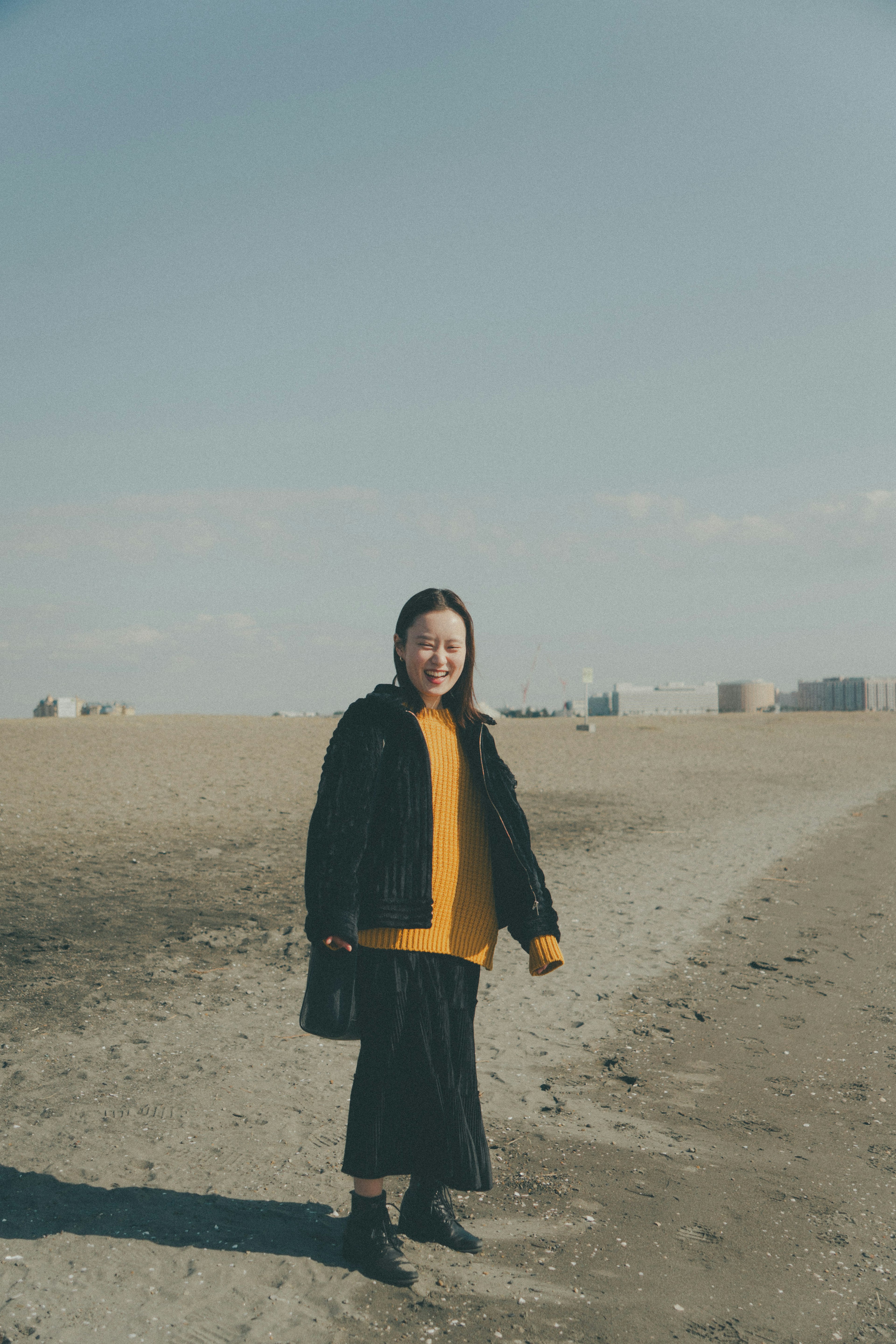 Eine lächelnde Frau steht an einem Sandstrand unter einem blauen Himmel