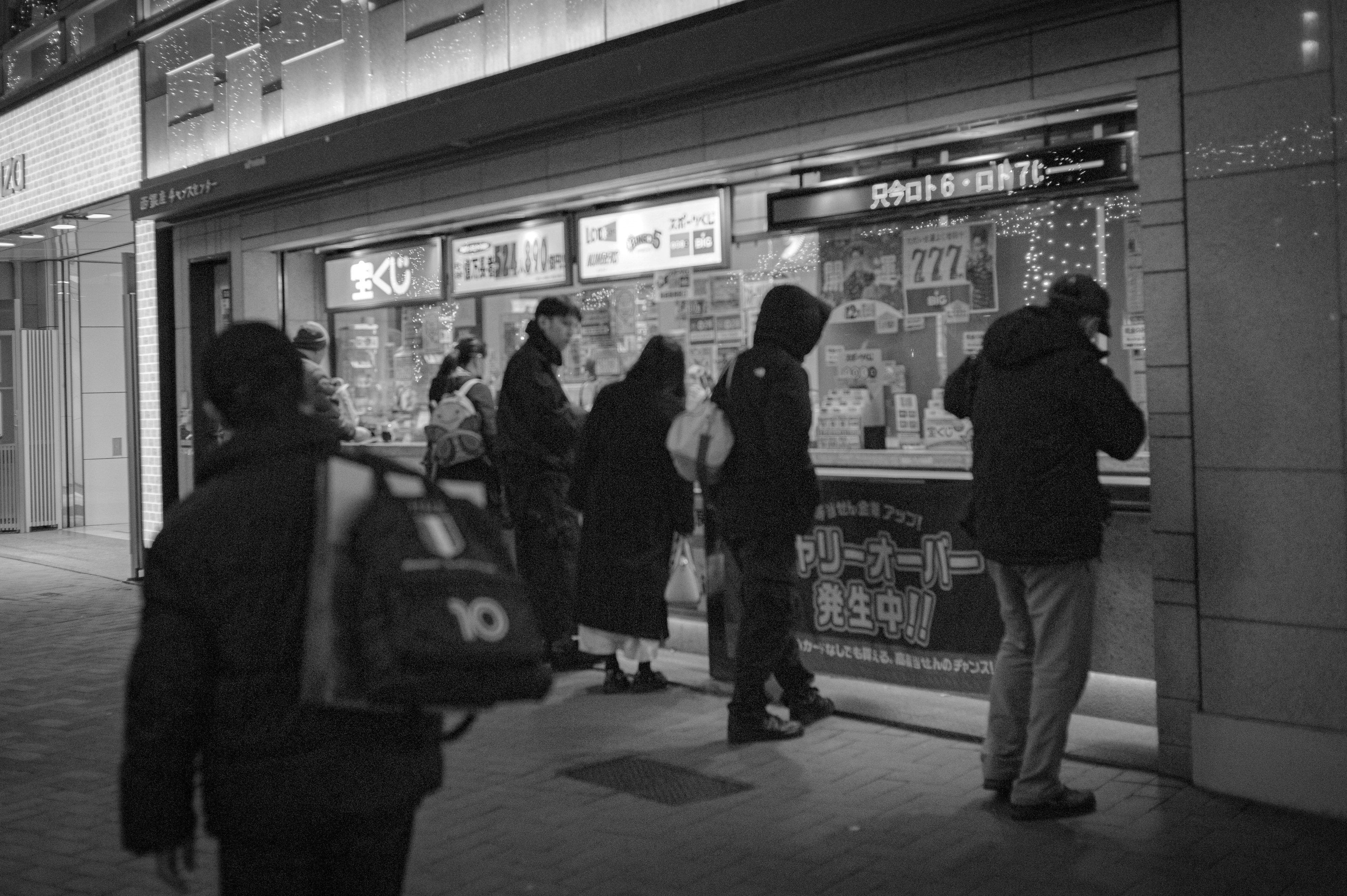 Black and white scene of people looking at a menu outside a shop at night