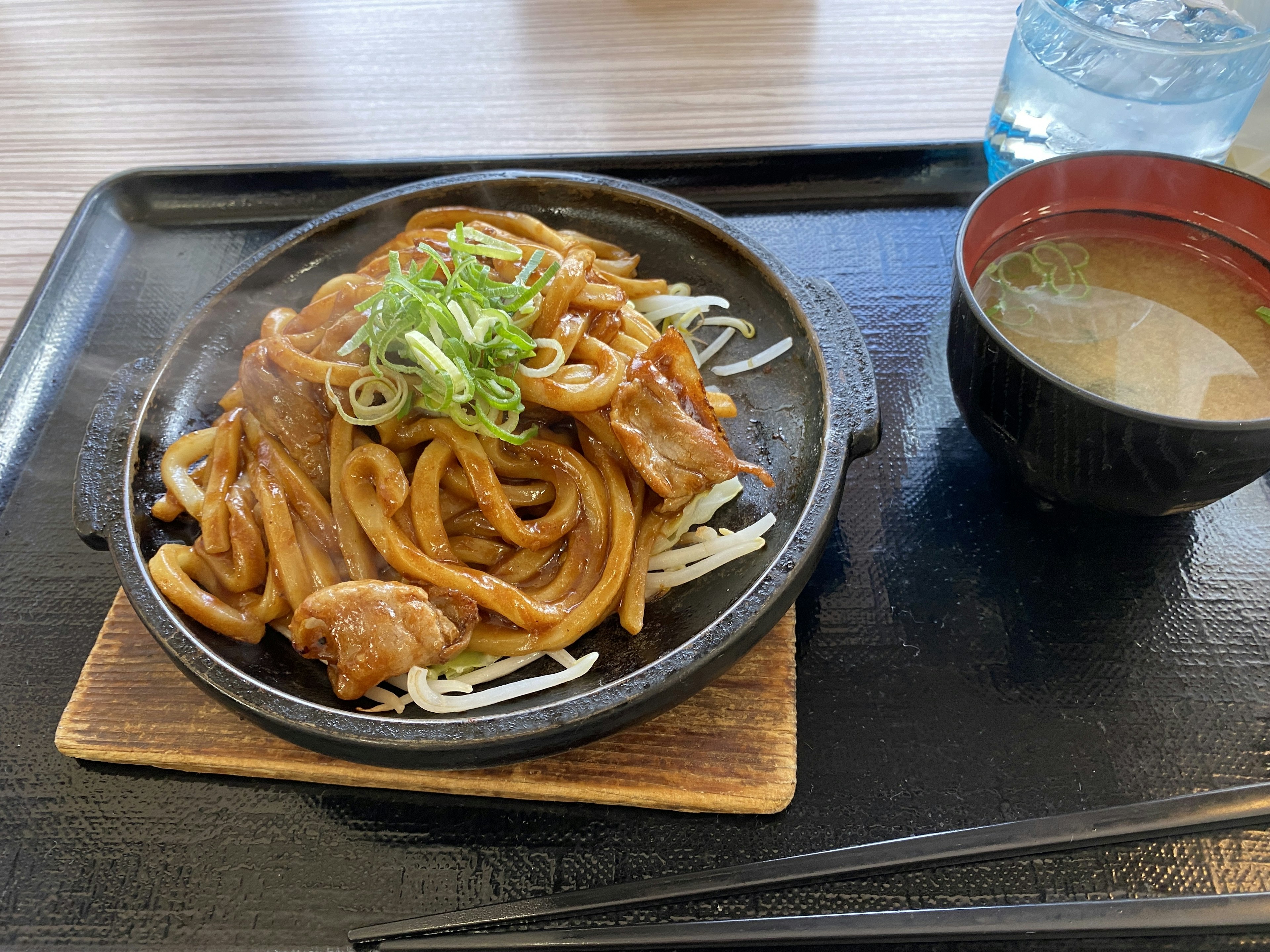 鉄板で提供されるうどんと肉の料理 緑のねぎがトッピングされている