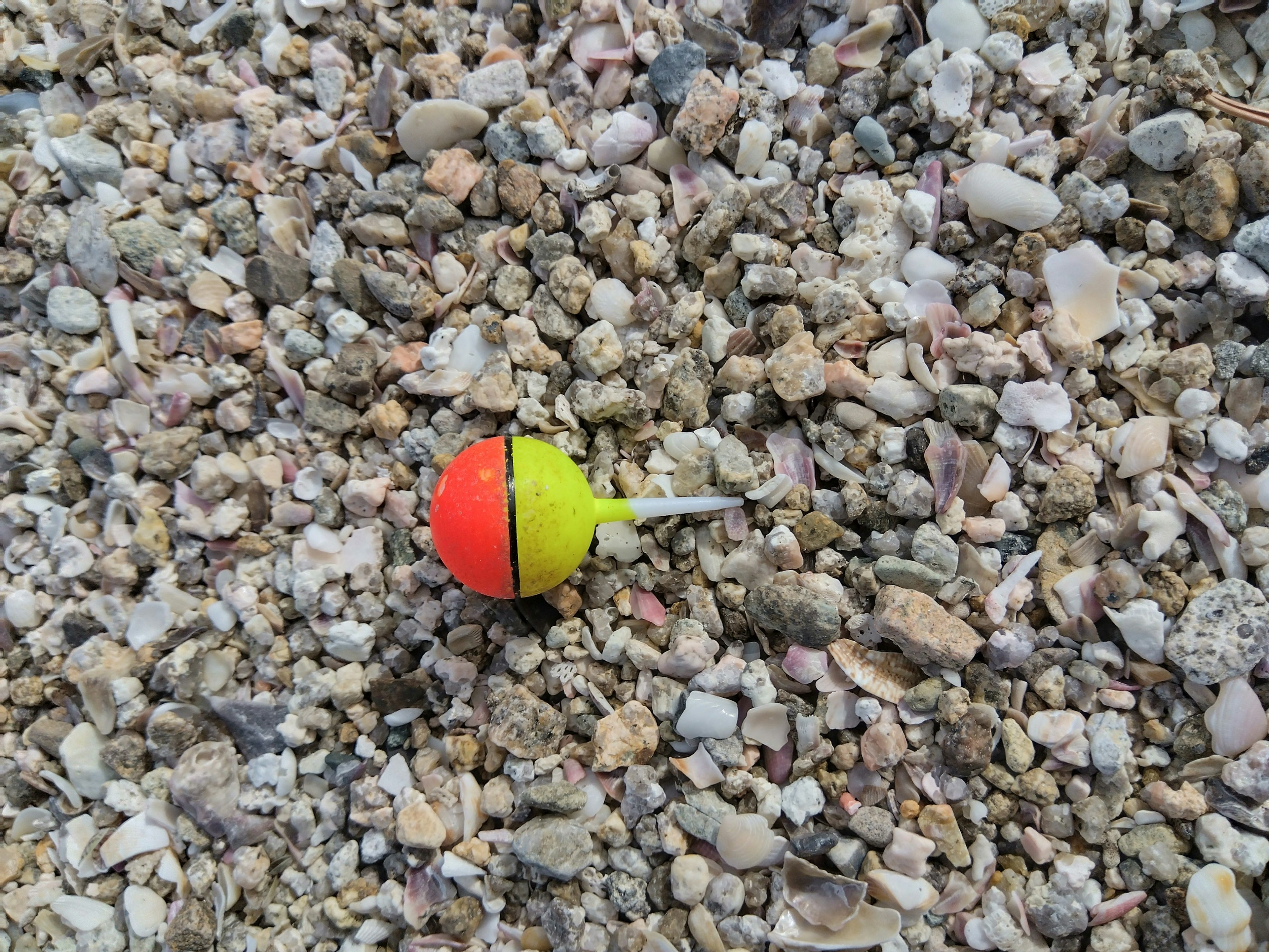 Red and yellow fishing bobber on gravel