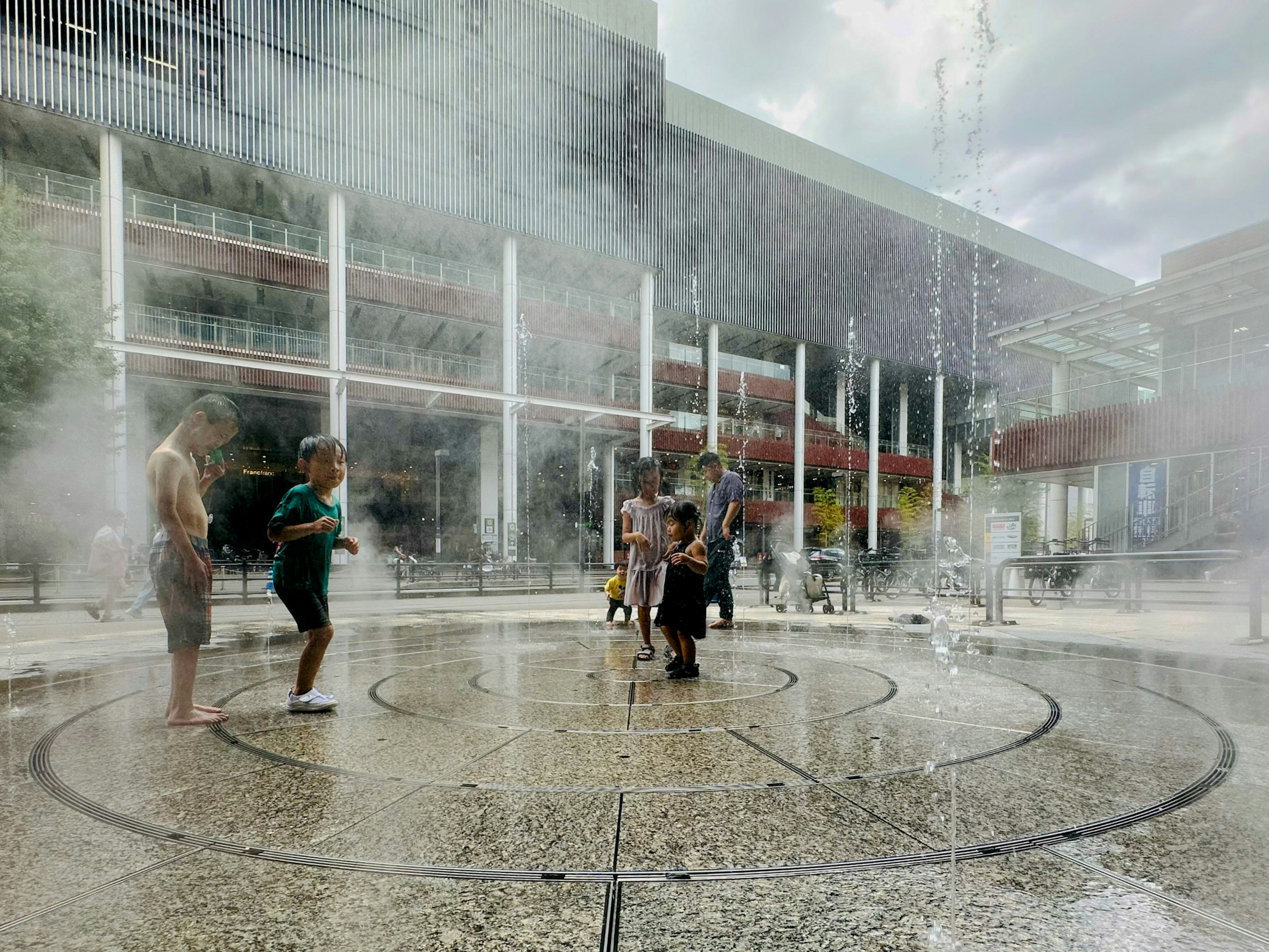 Children playing in a water fountain mist with a wet ground and a cloudy background