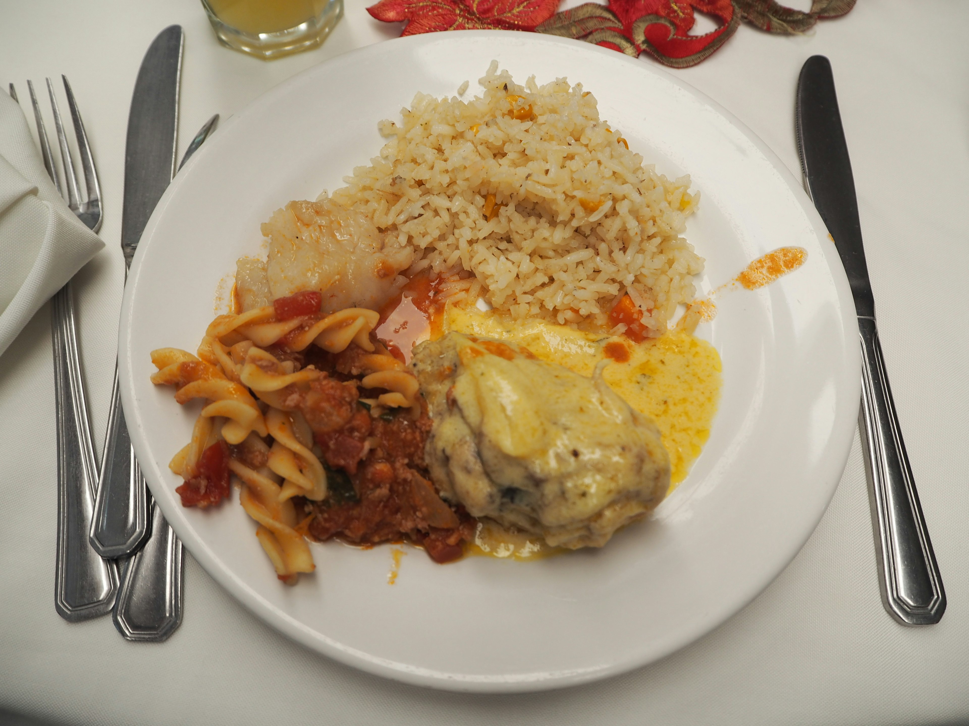 Ein Teller gefüllt mit verschiedenen Gerichten darunter Fleisch mit gelber Sauce Pasta mit Tomatensauce und Reis der wie Pilaf aussieht