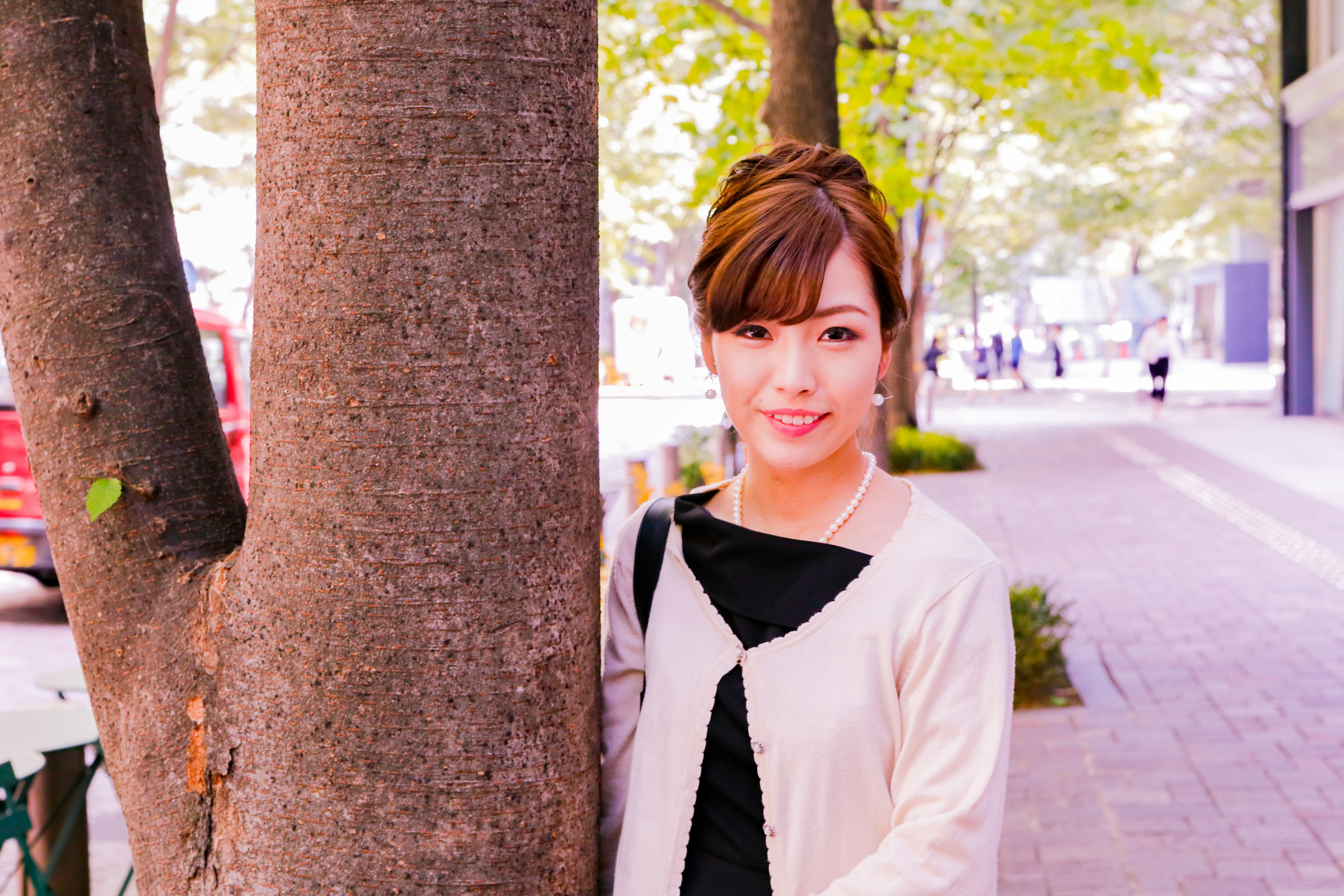 A woman smiling beside a tree in an urban setting