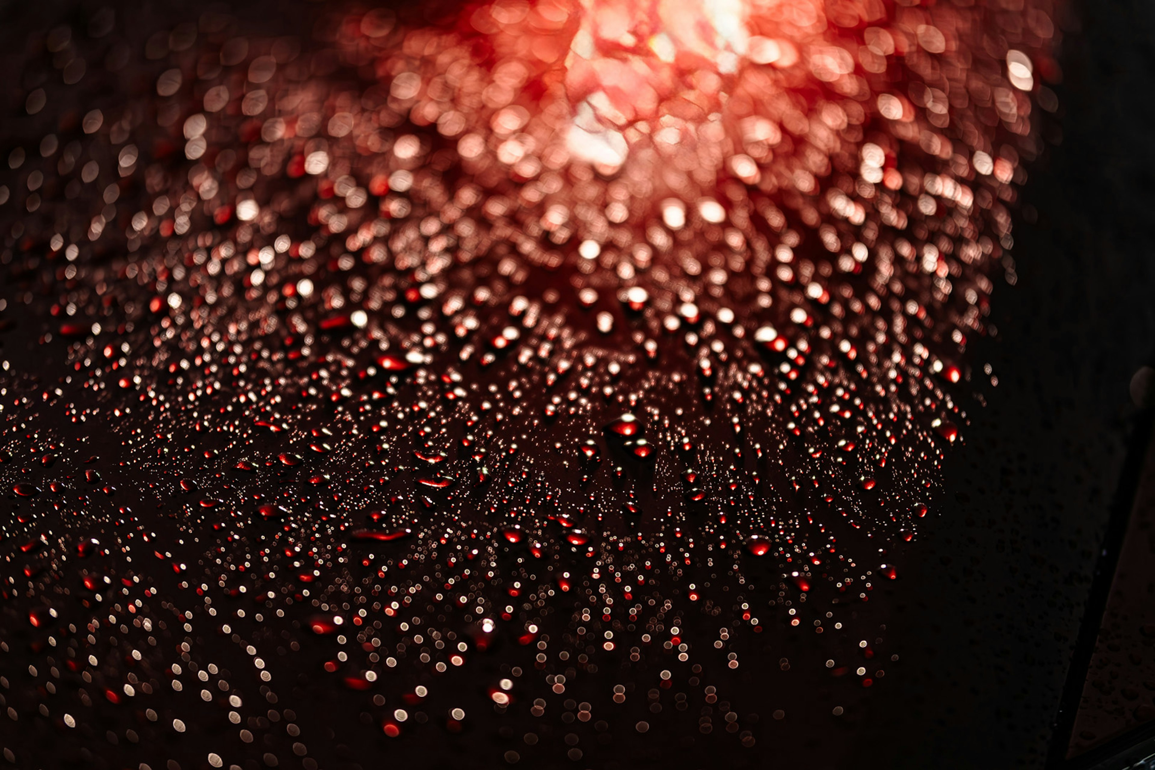 Superficie cubierta de gotas brillantes iluminadas por luz roja