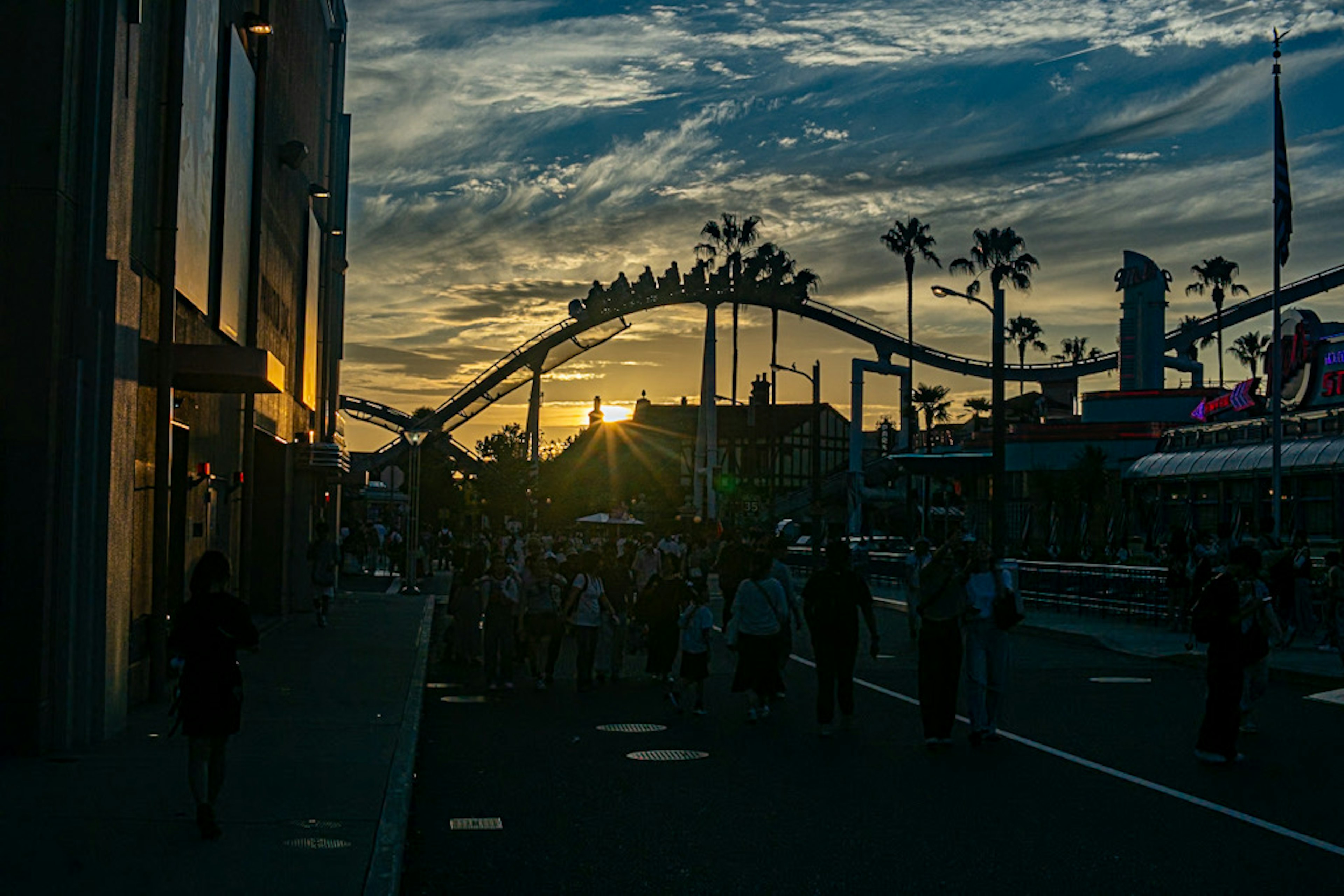 夕日を背景にした遊園地のシルエットと人々の群れ