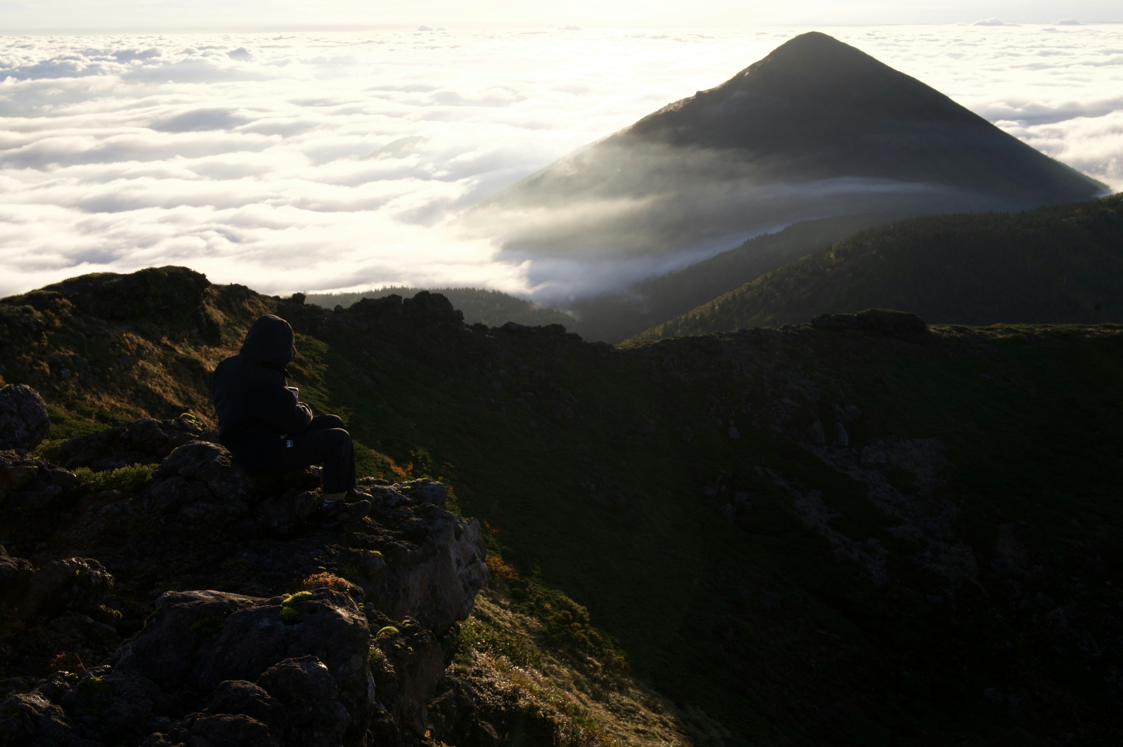 Silhouette seorang yang duduk di puncak gunung melihat lautan awan