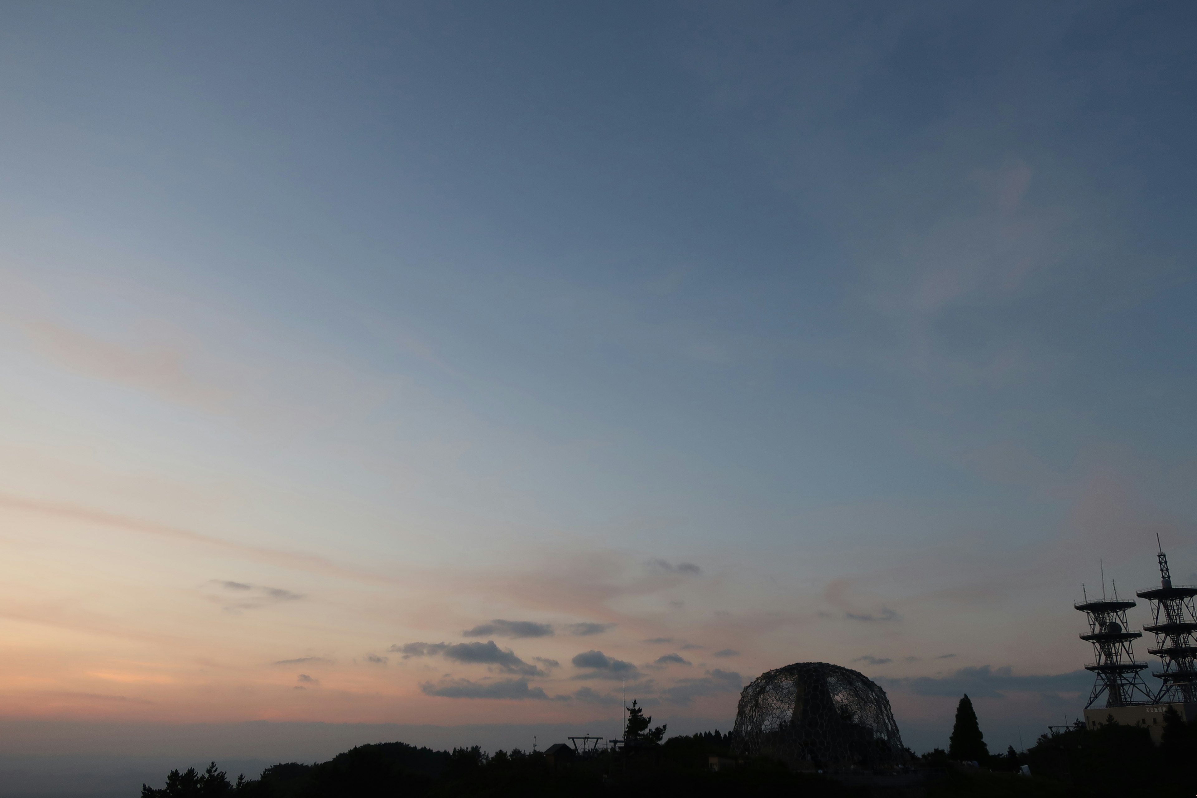 Ein Farbverlauf aus blauem Himmel und Sonnenuntergang mit silhouettierten Gebäuden und Bäumen