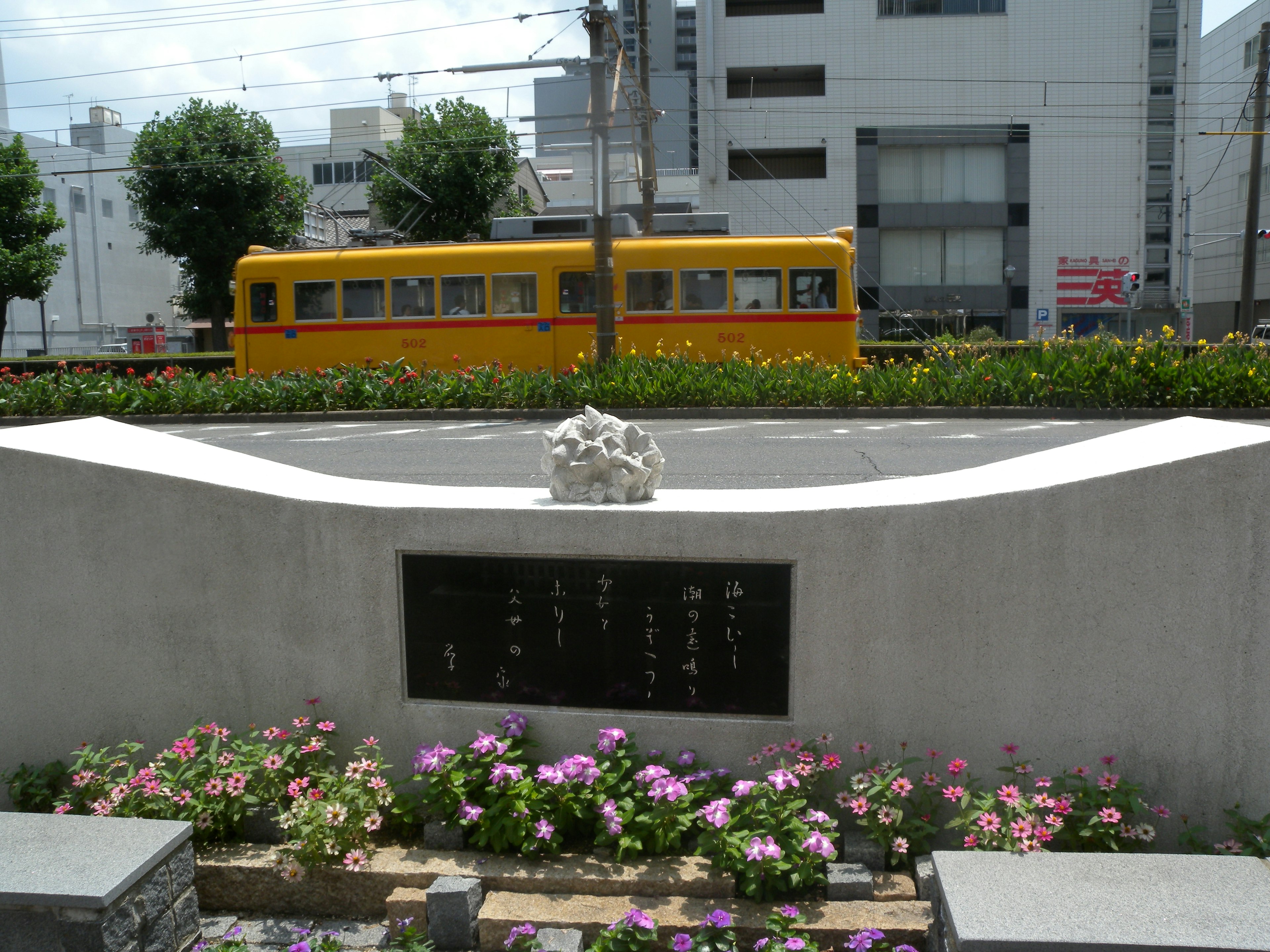 Monument avec des fleurs et un tram jaune en arrière-plan