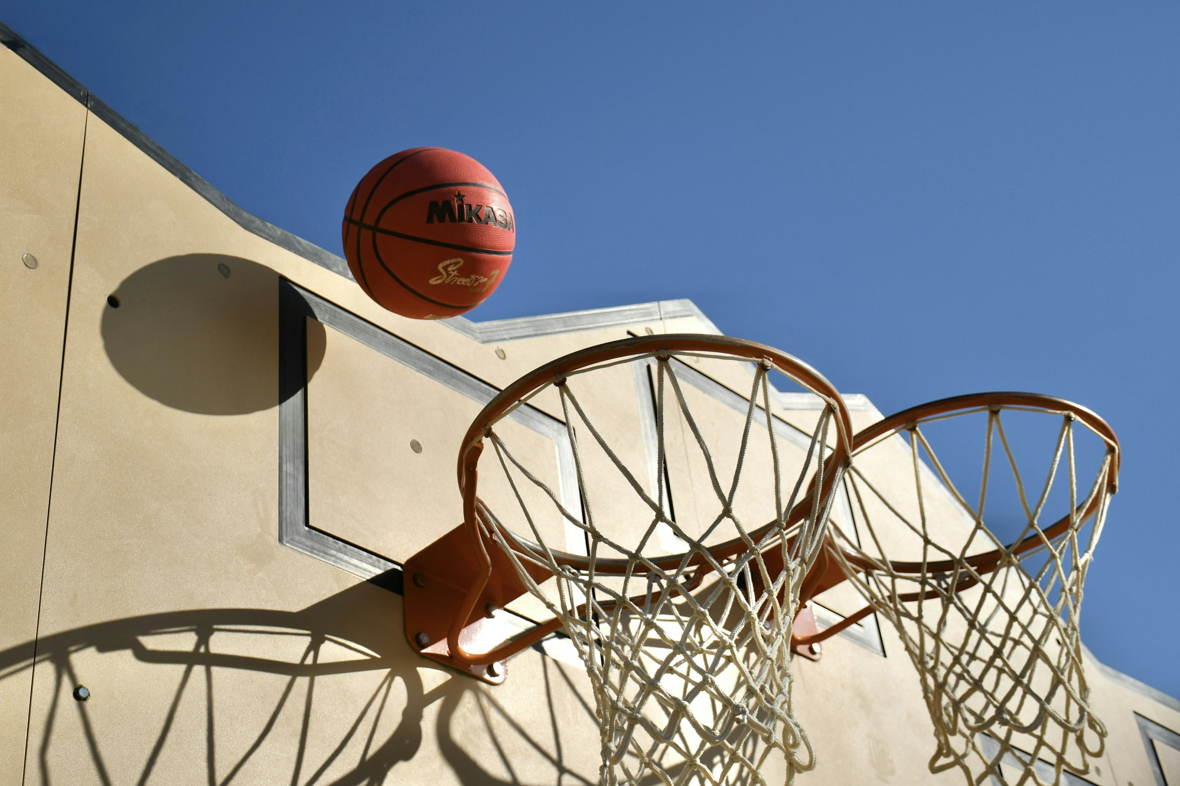 Un balón de baloncesto volando sobre dos aros de baloncesto bajo un cielo azul