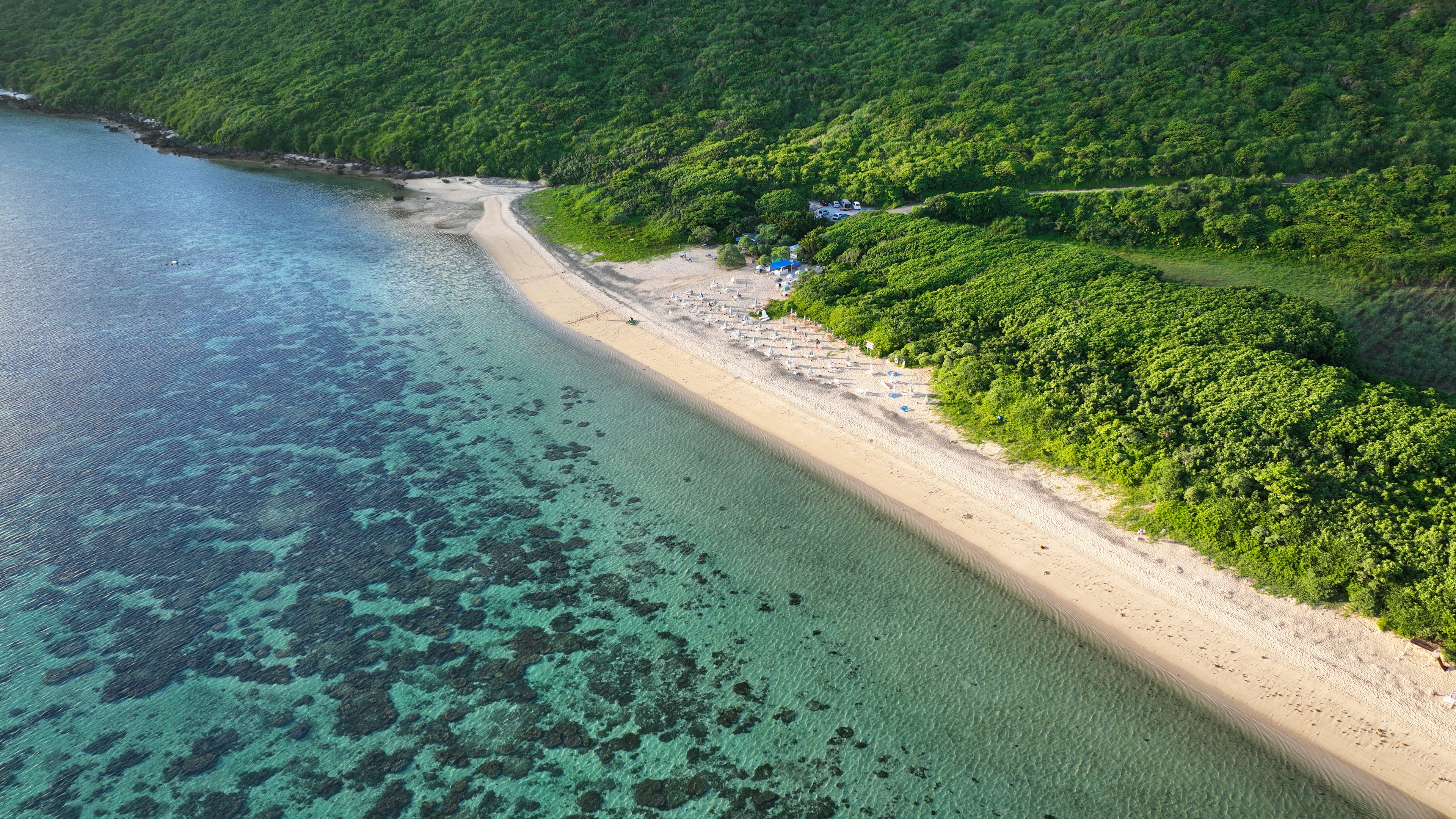 Aerial view of a beach surrounded by blue water and green hills