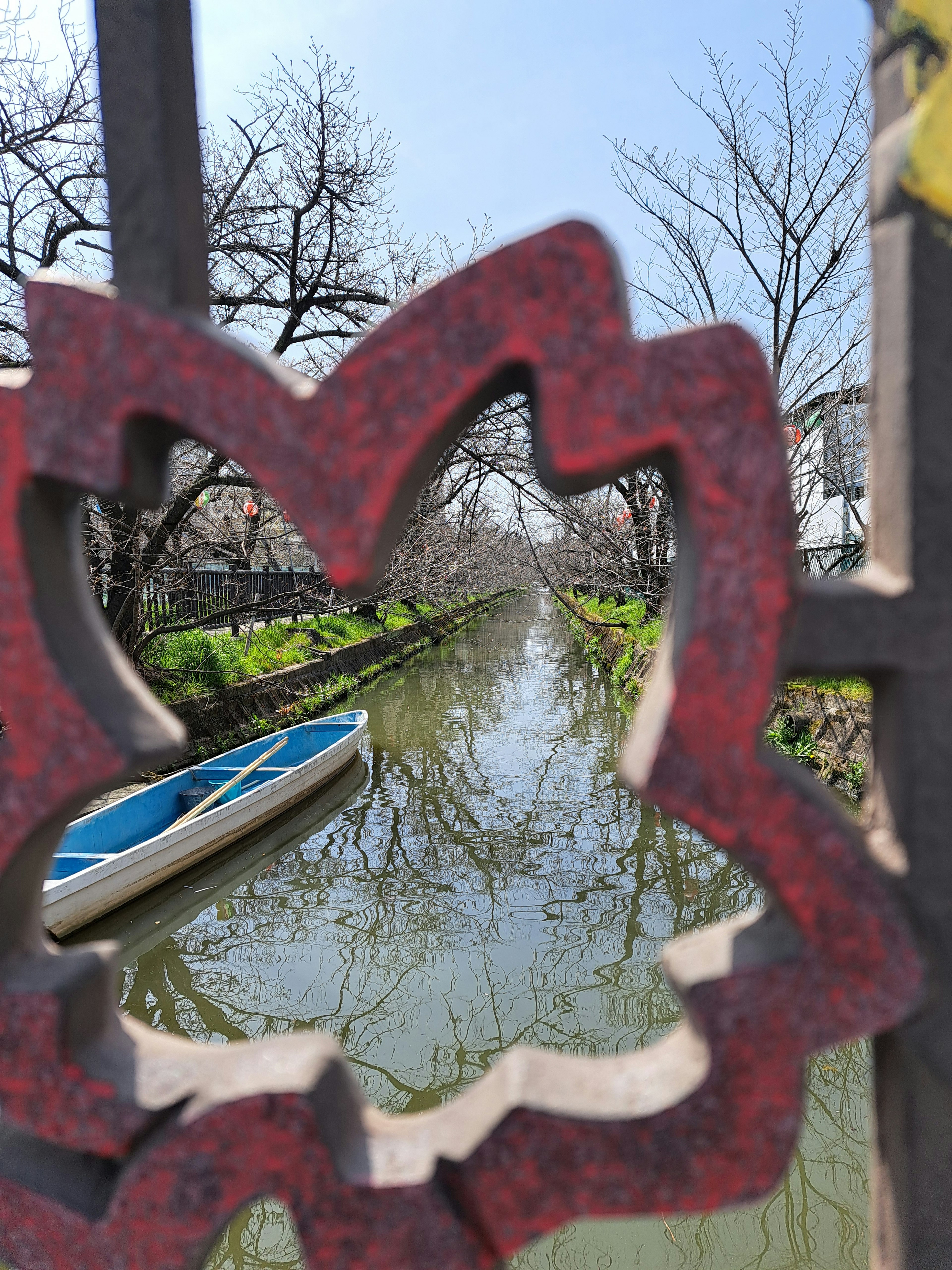 Blick durch einen roten blumenförmigen Zaun auf einen ruhigen Kanal und ein Boot