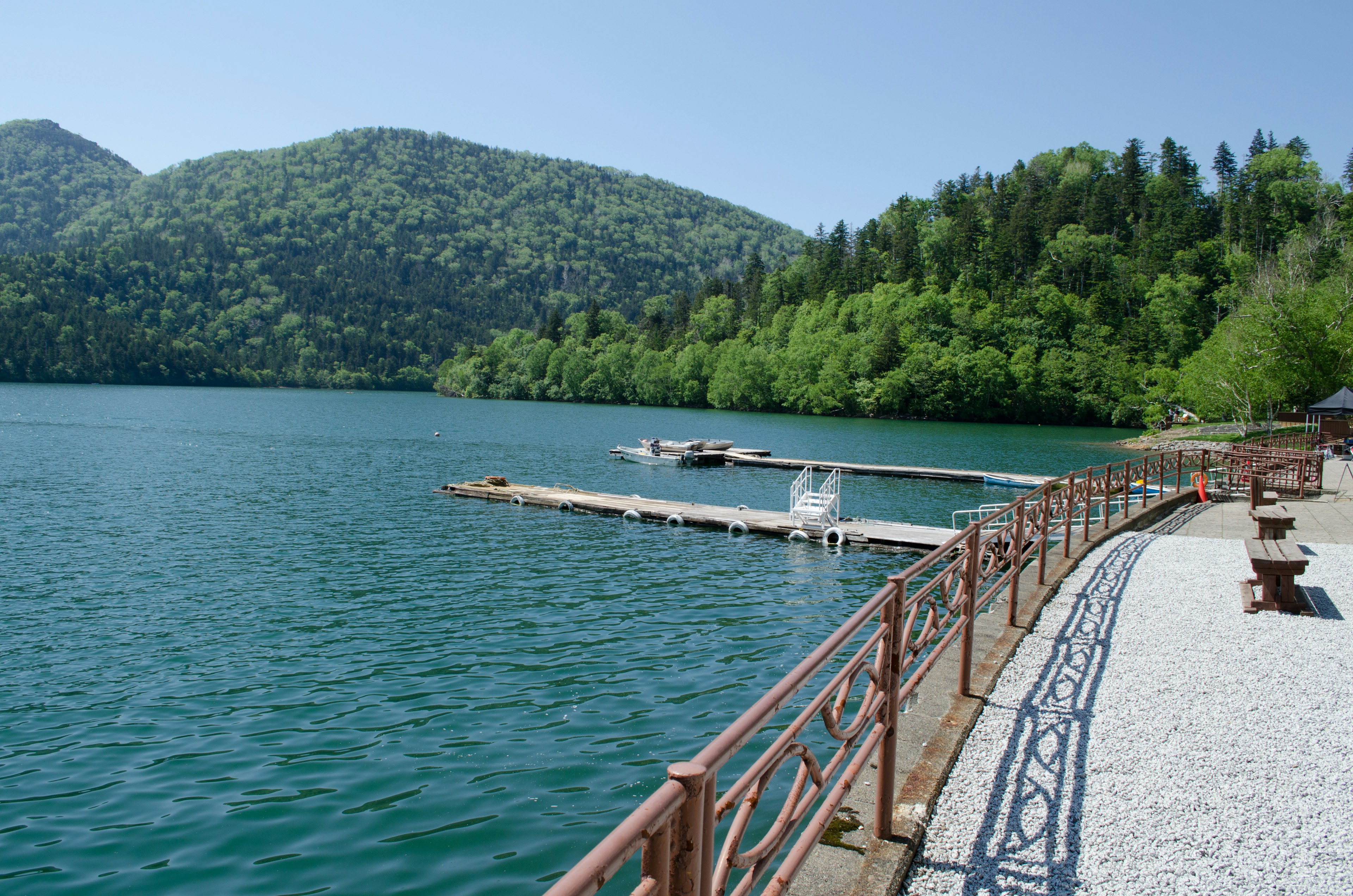 ทิวทัศน์ที่สวยงามของทะเลสาบที่สงบกับภูเขาสีเขียวด้านหลังที่มีท่าเรือและทางเดิน