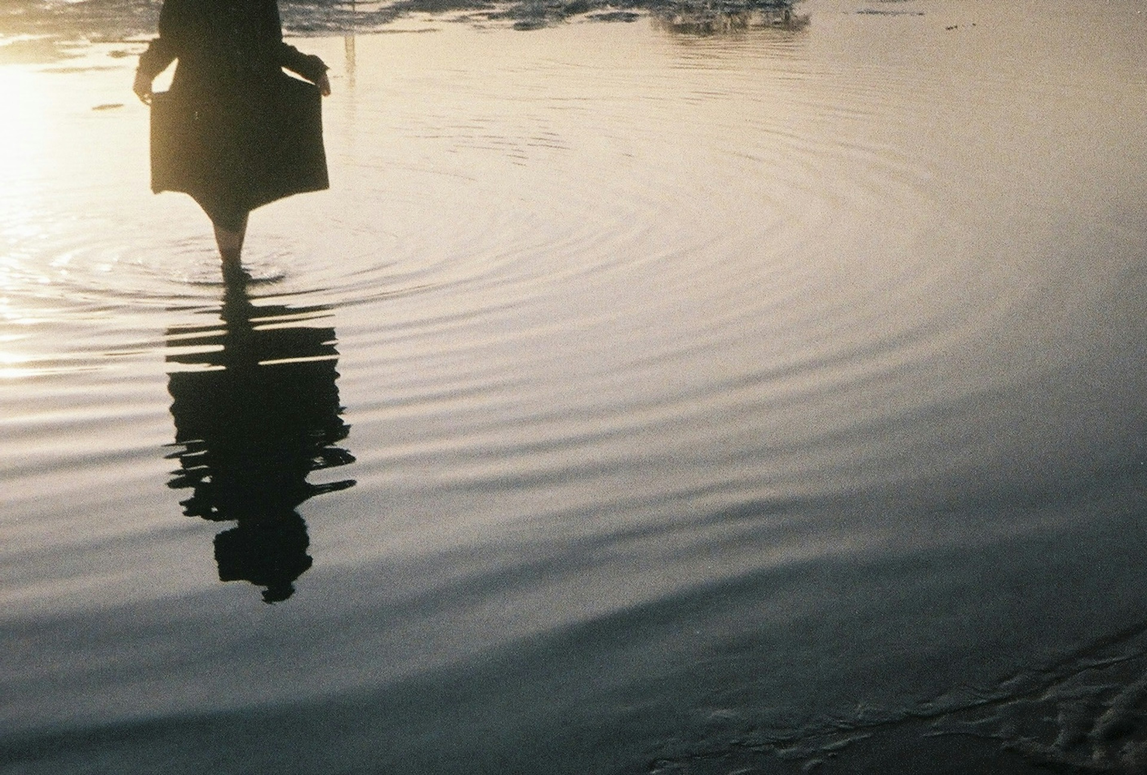 Silhouette d'une personne se tenant au bord de l'eau avec des ondulations à la surface